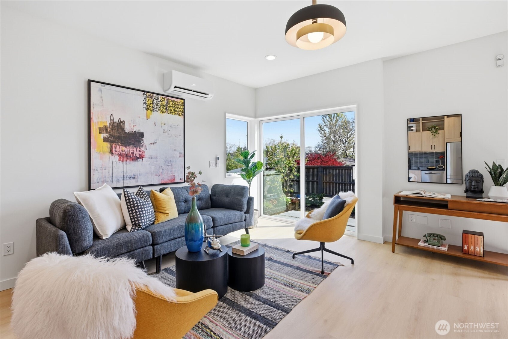 Bright open-concept living room with oversized windows, mini-split heating and cooling, natural light, and seamless access to private outdoor space.