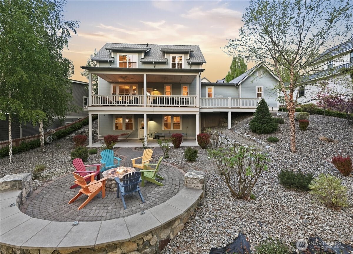 Exterior twilight view of west-facing outdoor living area with two level decks and custom stone fire pit with colorful Adirondack chairs overlooking the lake.