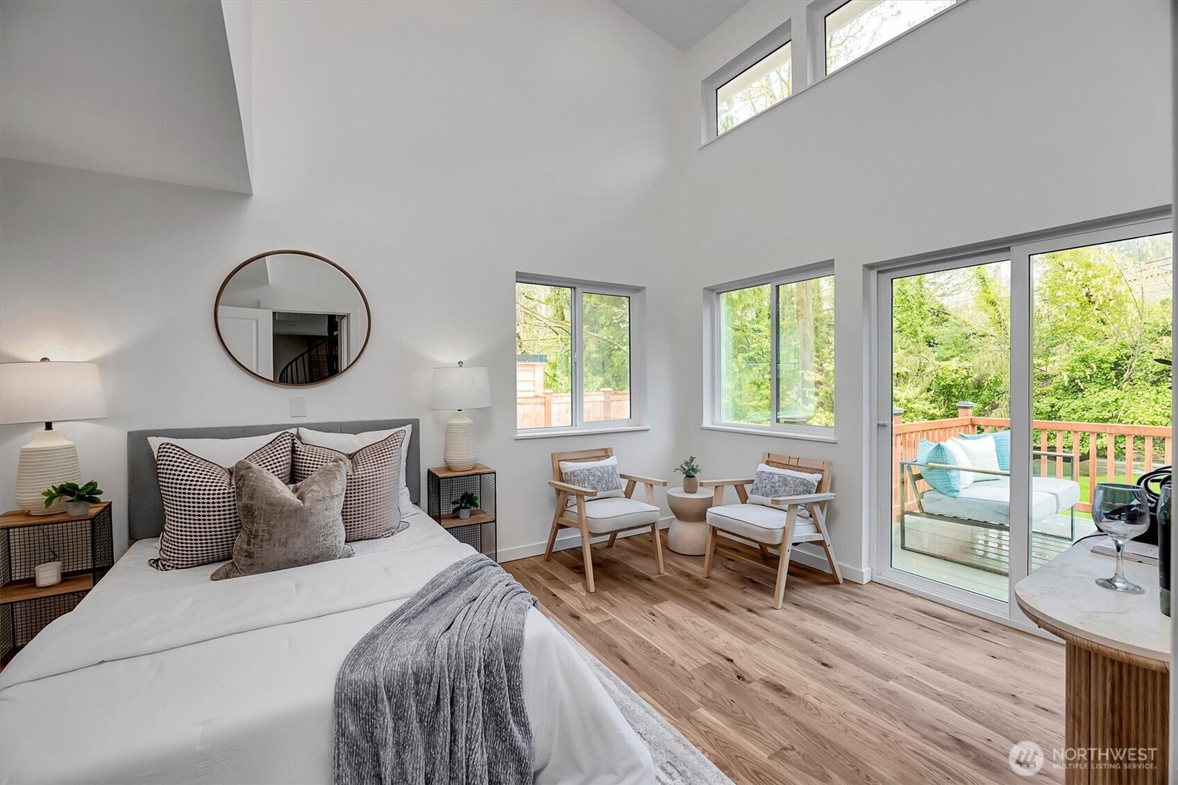 Breathtaking primary bedroom featuring soaring vaulted ceilings, walls of windows, and direct deck access overlooking a serene creek and wooded backyard and wide-plank hardwood laminate.