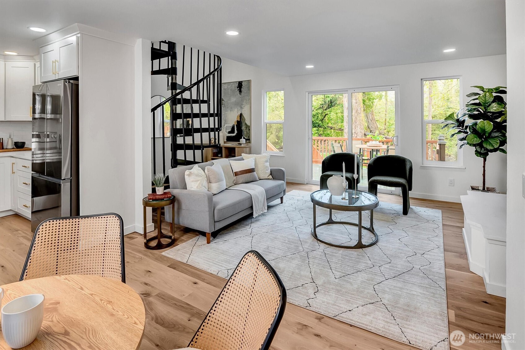 Living room featuring a wood-clad fireplace, laminate hardwood floors, and sliding glass doors opening to a deck with serene creek and tree-lined views.