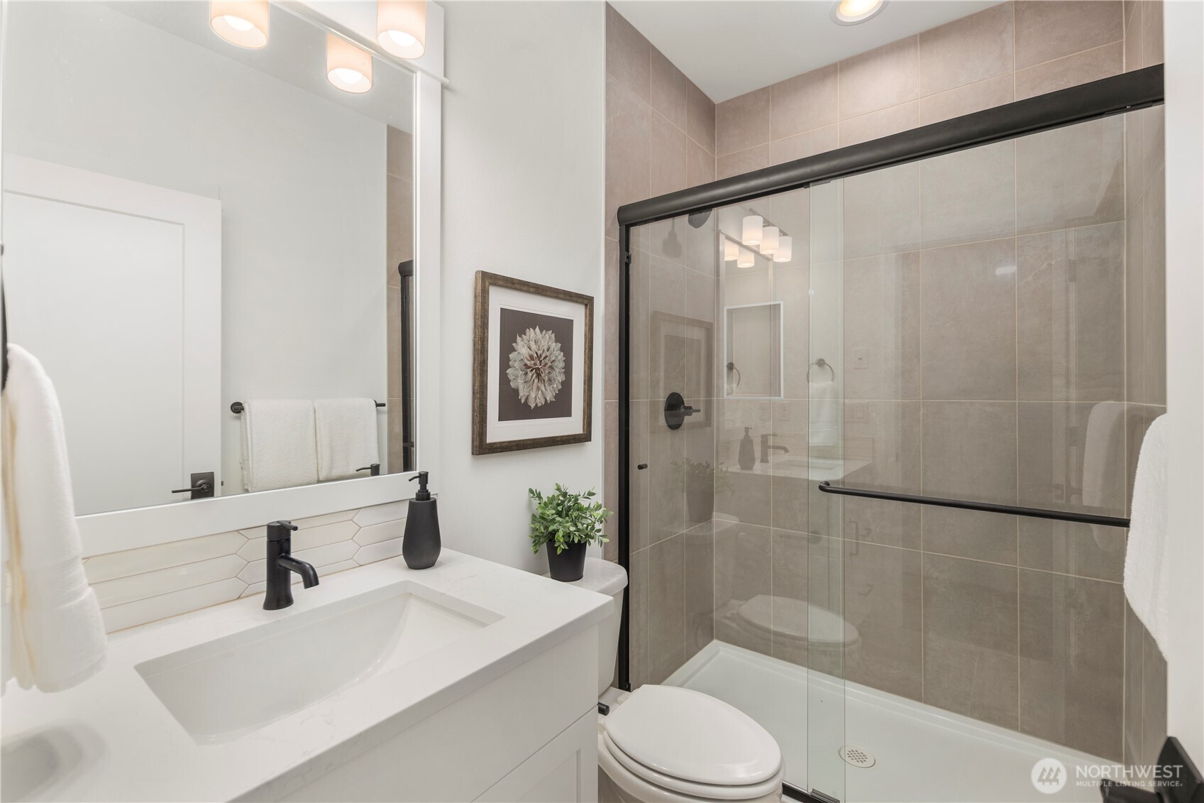 Main-Level Guest Bathroom:  This well-appointed bath features a wide quartz-topped vanity, soft neutral tilework, and a frameless glass shower enclosure accented with matte black hardware. Its thoughtful layout supports comfort and convenience for guests or main-level living. With Gooden Hollow’s Bothell location in the Canyon Park corridor, this space benefits from close proximity to parks, everyday amenities, and major commuter routes. Clean lines and modern fixtures bring a polished, cohesive feel to this main-floor bath.    These photos are from Lot 5 at Gooden Hollow, the community model. The home listed will have changes, so all photos, renderings, site maps, and floorplans are for visualization purposes only. Plans, colors, building orientation, finishes, home outlook, and other details can and WILL vary.