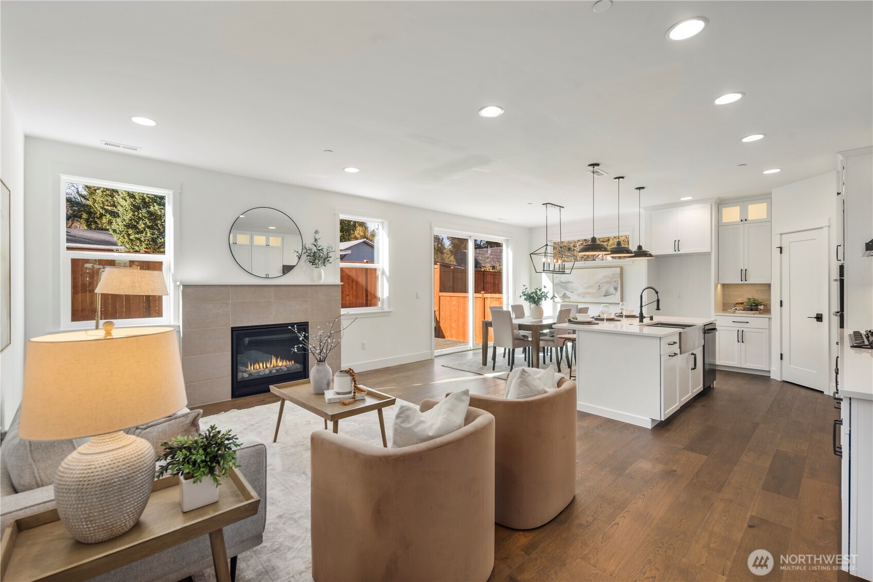 Great Room:  Large windows spill natural light across the great room, highlighting the wide-plank flooring and the gas fireplace wrapped in soft neutral tile. The open flow invites flexible furniture placement and comfortable day-to-day living. With Gooden Hollow’s Bothell location near Canyon Park amenities, this room becomes a peaceful backdrop to Northwest living, surrounded by mature evergreens and convenient access to nearby recreation. Its simplicity and warmth make it equally suited for quiet evenings or effortless entertaining.    These photos are from Lot 5 at Gooden Hollow, the community model. The home listed will have changes, so all photos, renderings, site maps, and floorplans are for visualization purposes only. Plans, colors, building orientation, finishes, home outlook, and other details can and WILL vary.