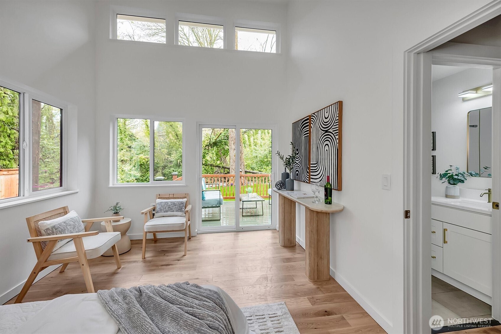 Breathtaking primary bedroom featuring soaring vaulted ceilings, walls of windows, and direct deck access overlooking a serene creek and wooded backyard and wide-plank hardwood laminate.