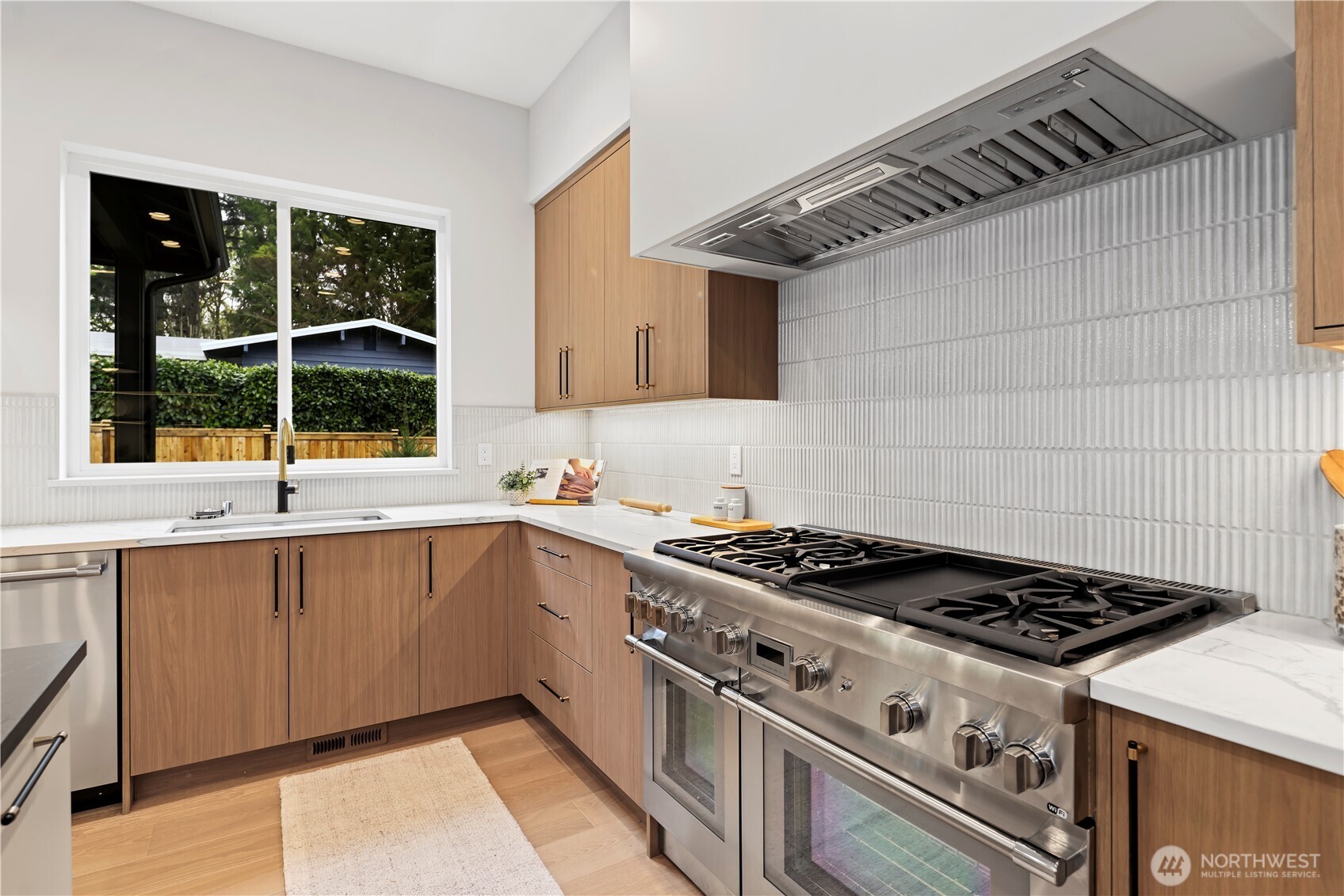 Thermador range with custom-framed hood. 6-burner, griddle, double ovens, and Wi-Fi enabled. Single-basin stainless steel sink with pull-out sprayer.