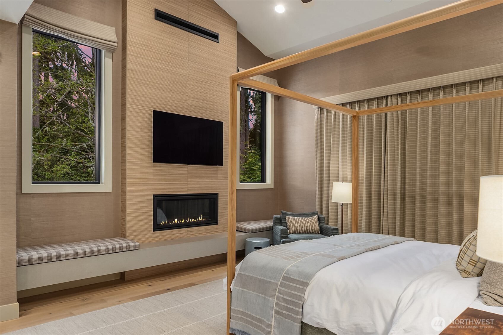 Fireplace glowing, drapery drawn, treetop views just beyond the glass. The kind of bedroom where a Sunday morning stretches into afternoon and nobody complains.