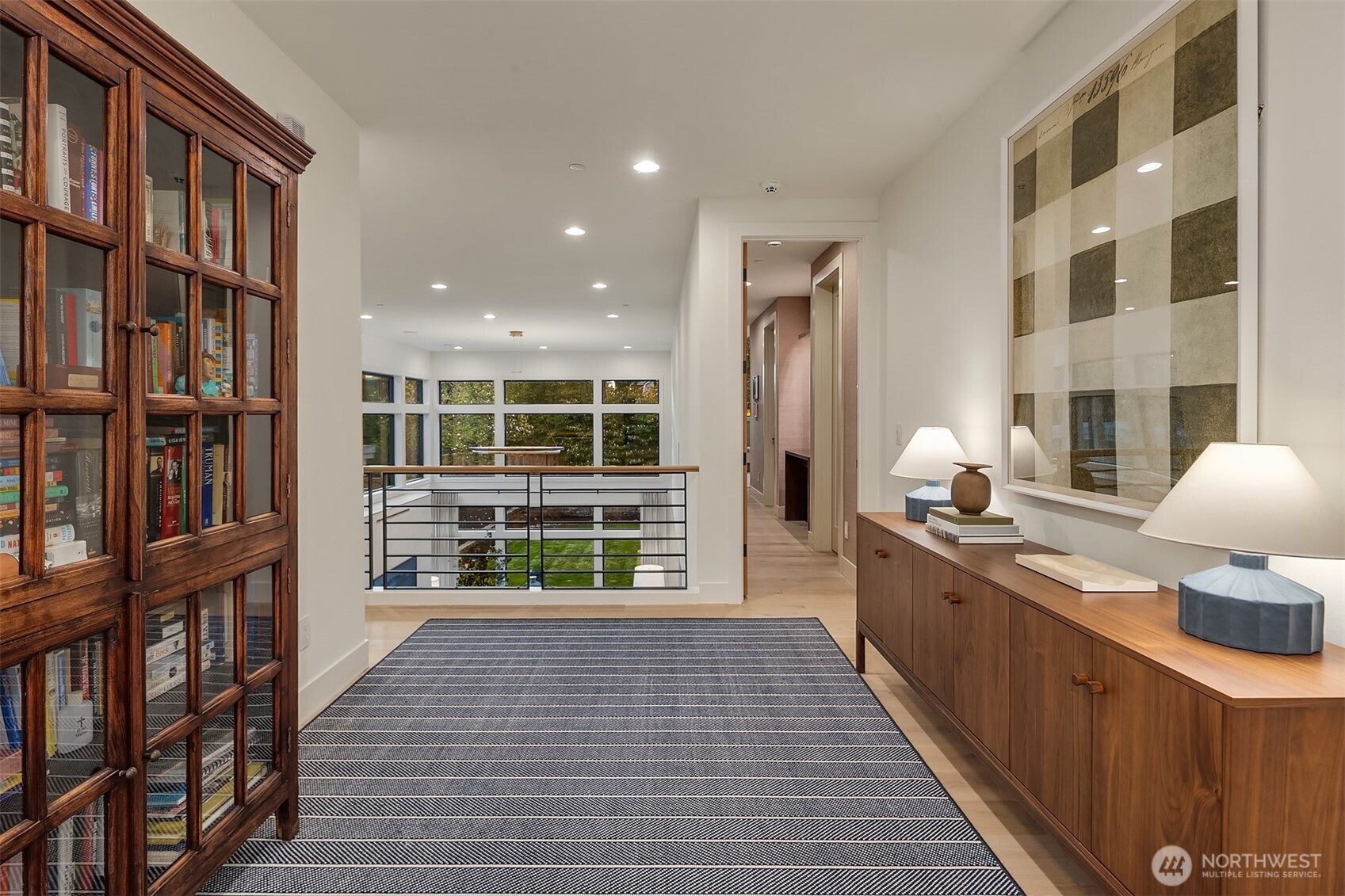 A wide-plank upper landing with steel railings, tree views, and the kind of thoughtful detailing that makes a hallway feel like part of the home — not just the space between rooms.