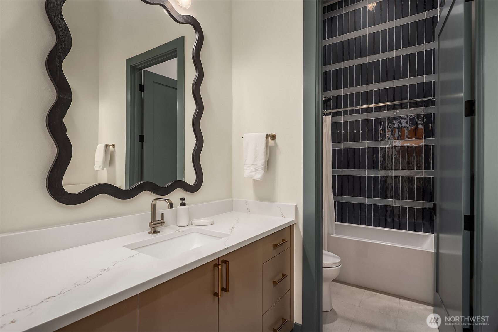 A sculptural mirror, deep navy vertical tile, quartz countertop, and heated floors.