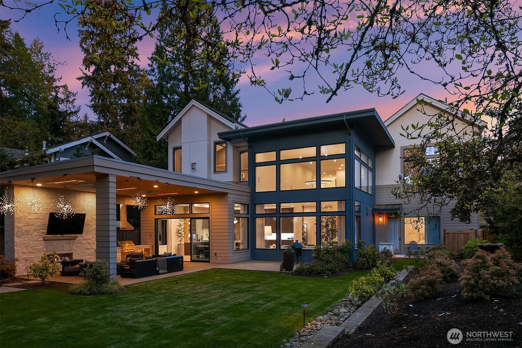 Soaring two-story window wall, cedar-clad terrace, and a glowing interior visible through every pane. The kind of exterior that stops you before you've even walked inside.
