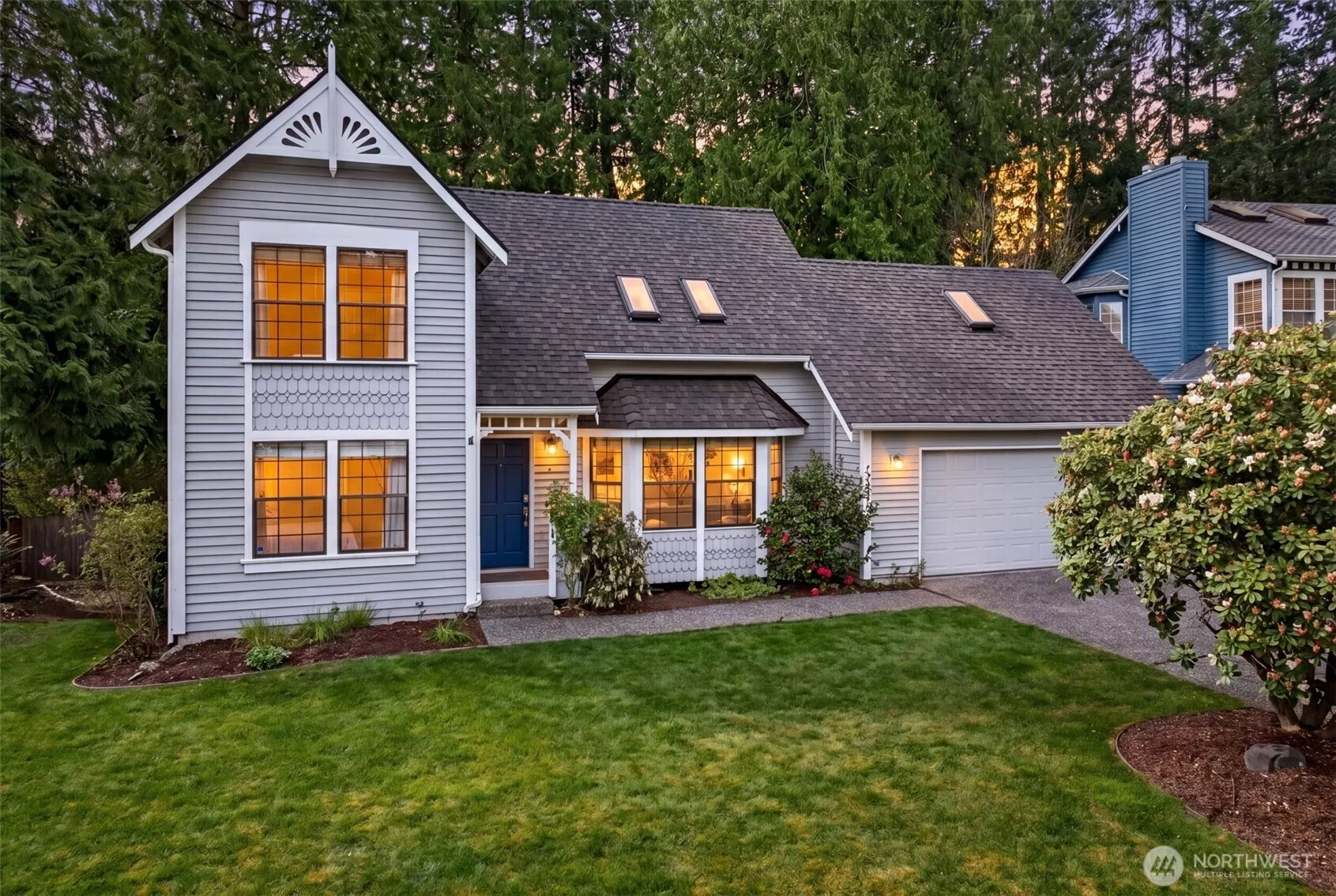 As dusk settles over Sunrise on English Hill, warm interior light spills through detailed windows, showcasing the home's character architecture against a backdrop of towering evergreens.