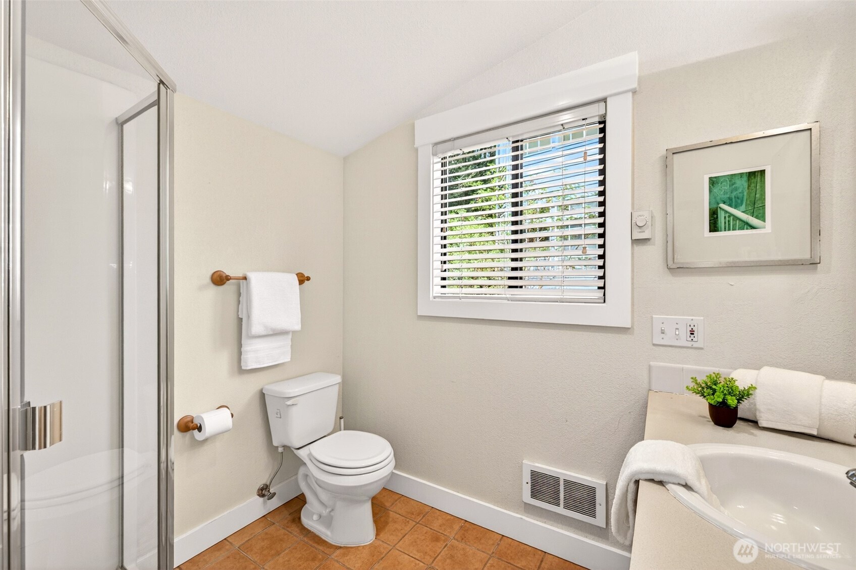 A convenient three-quarter bath on the main level features a glass-enclosed shower and bright window, ideal for guests or post-garden cleanup.