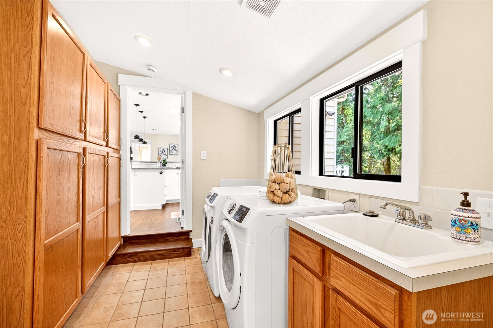 A spacious dedicated laundry room with side-by-side washer and dryer, deep utility sink, abundant cabinetry, and natural light keeps everyday chores organized and out of sight.
