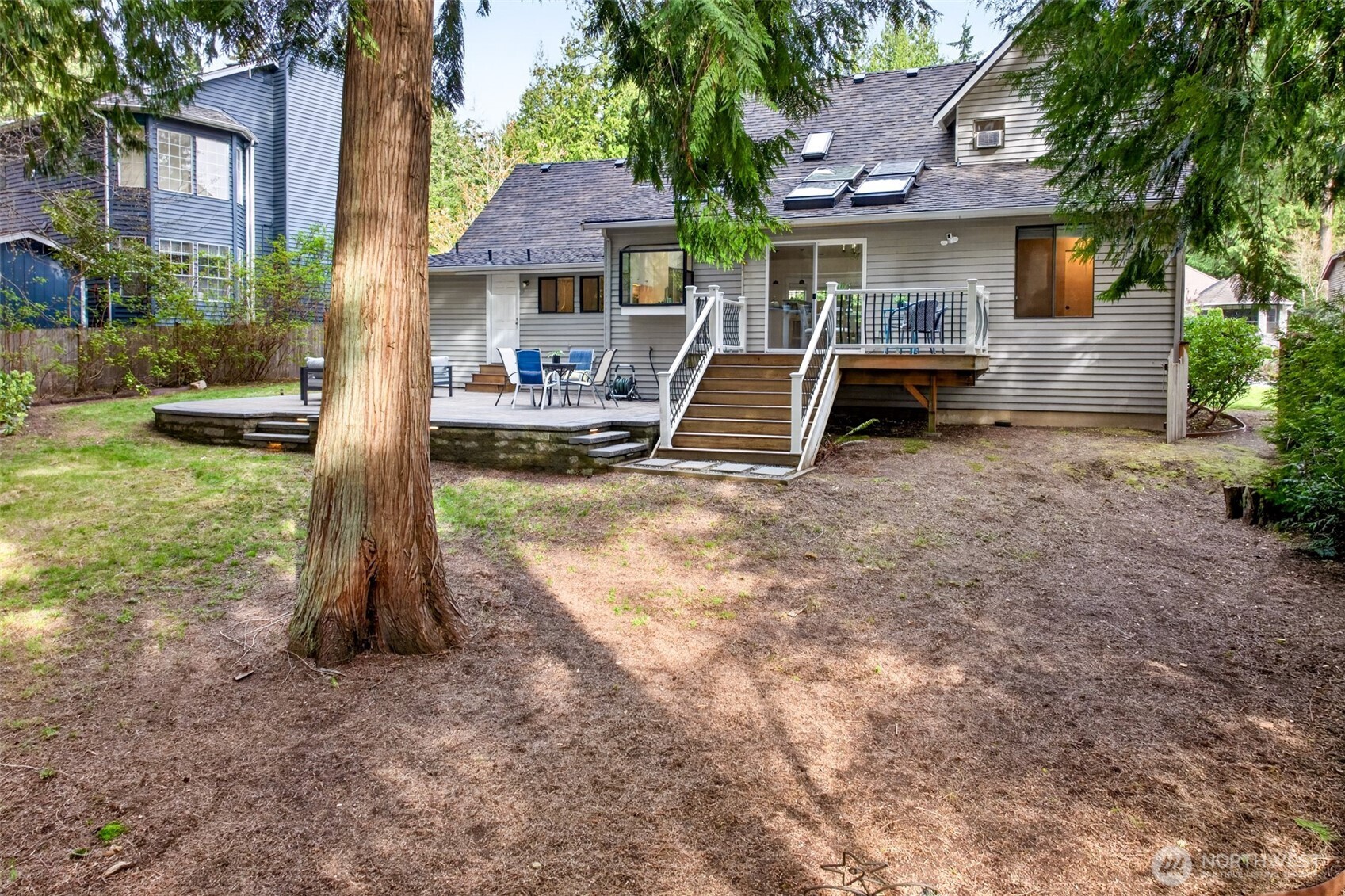 Stately cedar trees frame the rear yard, providing a natural canopy and serene backdrop while the elevated deck and patio create a seamless transition from indoor to outdoor living.