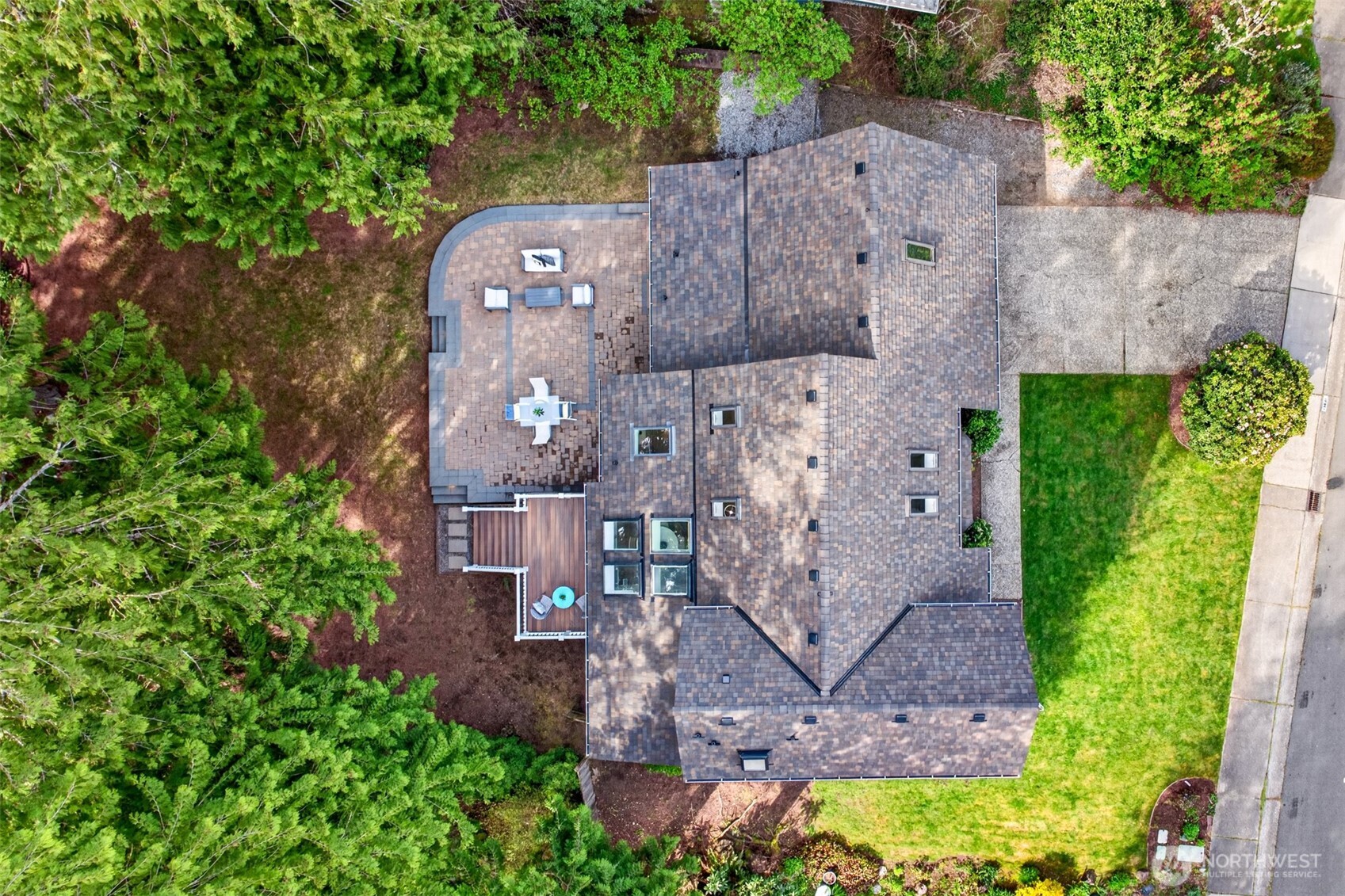 An overhead view captures the home's smart footprint, the substantial new paver patio with deck extension, and the wooded buffer wrapping the back of the lot.