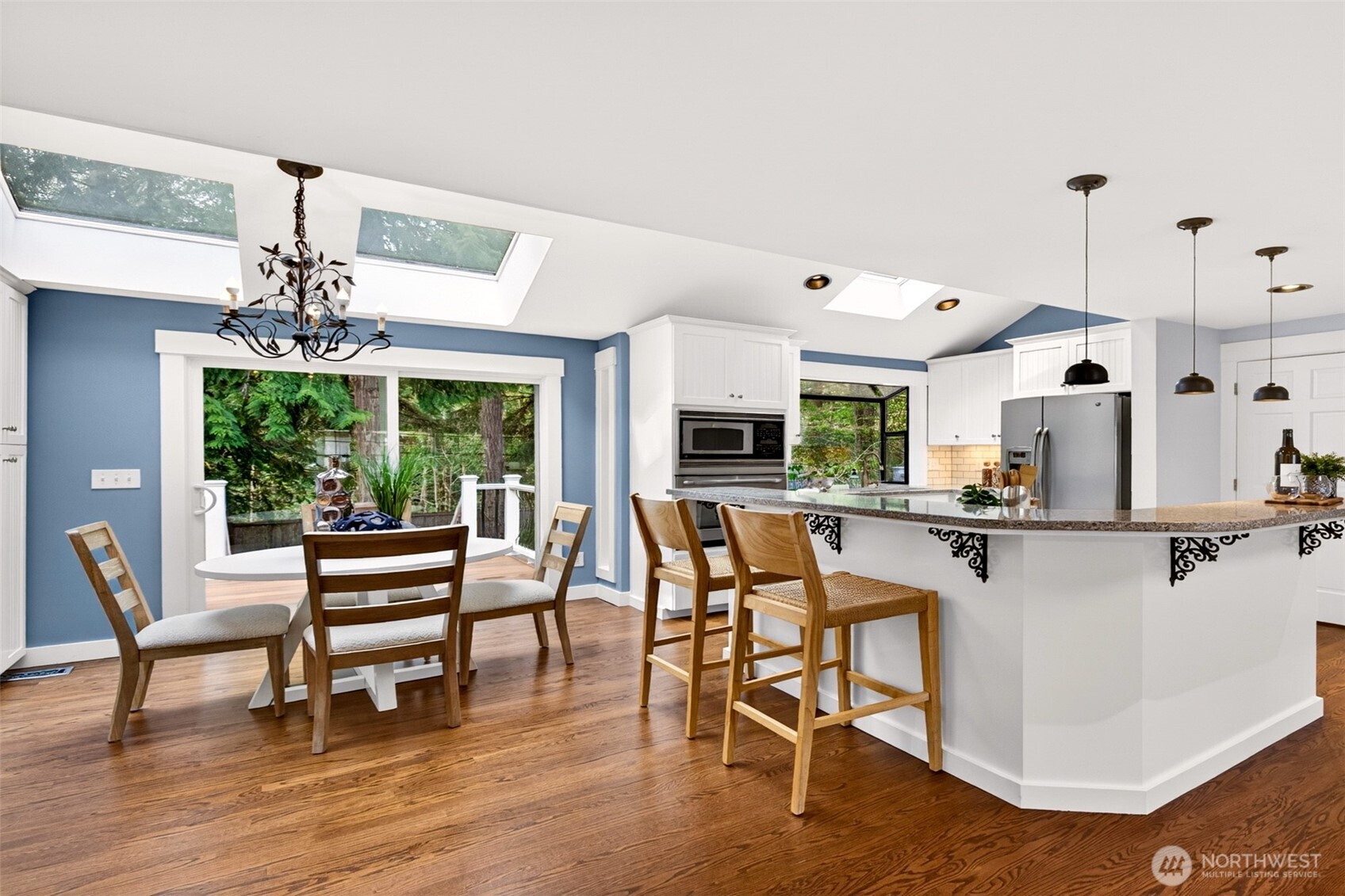 Vaulted ceilings, dual skylights, and a glass sliding door to the back deck bathe the dining nook and updated white kitchen in natural light, creating a bright, airy hub for daily life.