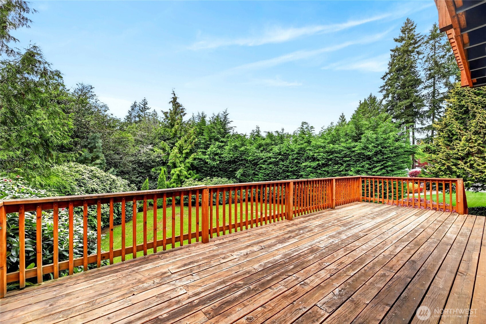 28’ view deck with serene views of mature rhodies and cedars. And steps leading to rear yard with lush green grass.