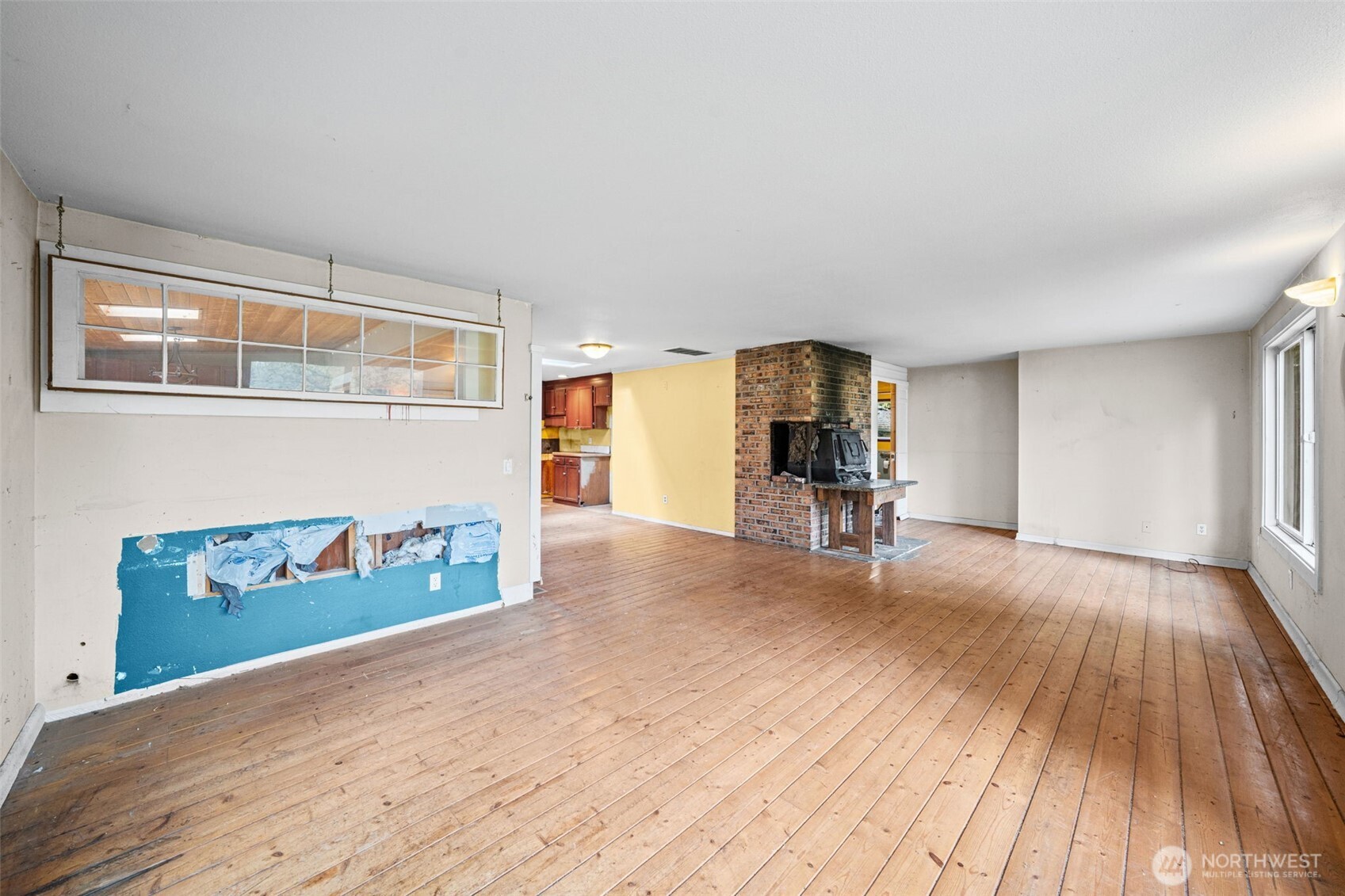 Expansive living room with hardwood floors and a statement brick fireplace as the focal point. Open layout offers incredible potential to create a warm, inviting gathering space.