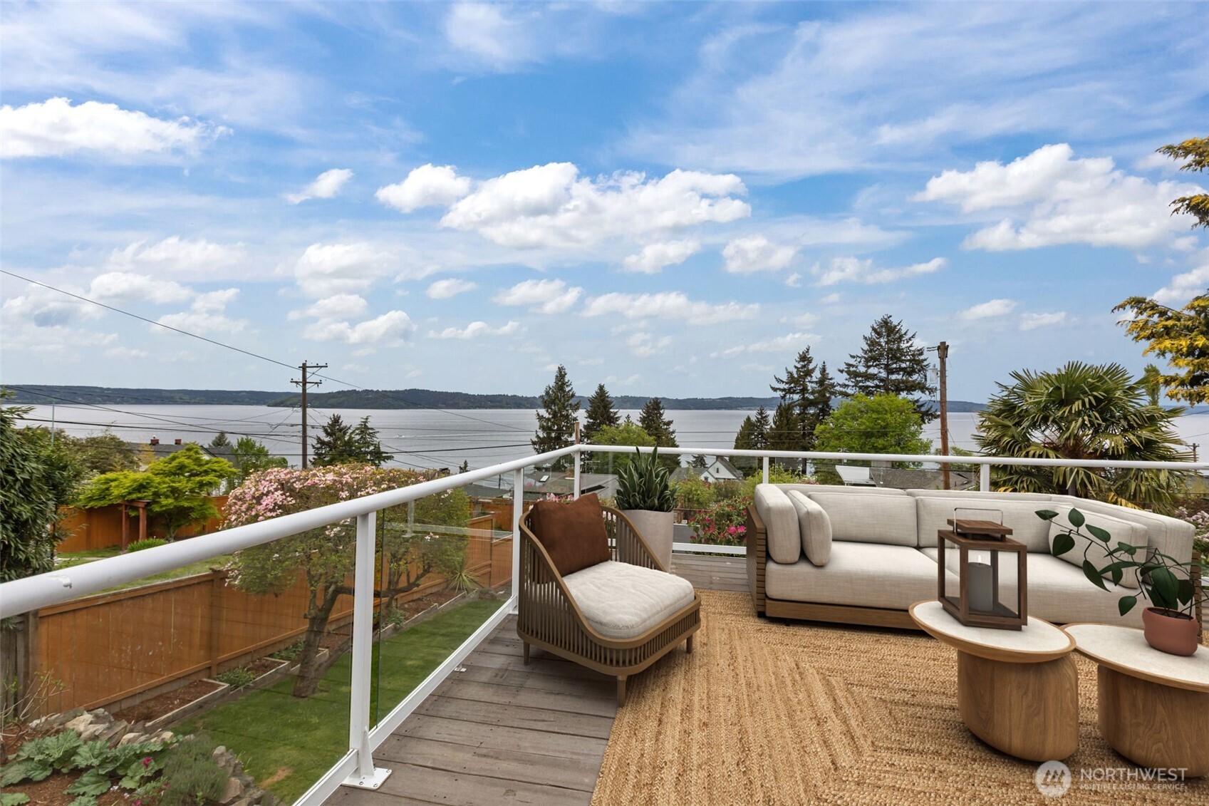 This outlook captures a broad sweep of open water, not just a narrow inlet—giving a true sense of scale and distance. You can see shoreline neighborhoods, forested hills, and distant landforms across the water, creating layered visual depth that changes throughout the day.