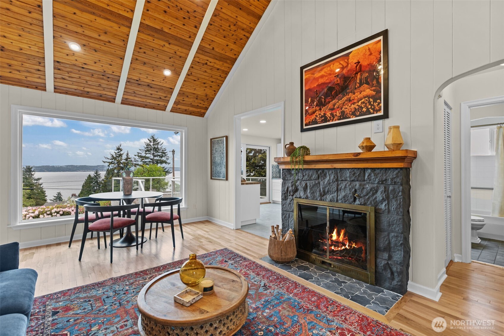 Vaulted tongue-and-groove wood ceilings. The warm cedar ceiling with exposed beams is a hallmark of Pacific Northwest cottage design, bringing natural texture indoors and echoing the surrounding landscape.