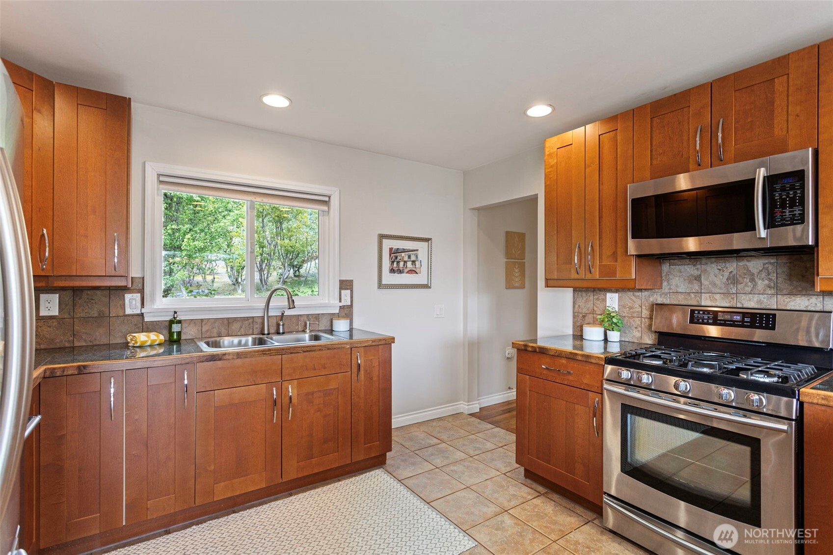 A double stainless sink is situated strategically under the large kitchen, with a touch faucet, tiled backsplash, under-cabinet lighting and stainless appliances.