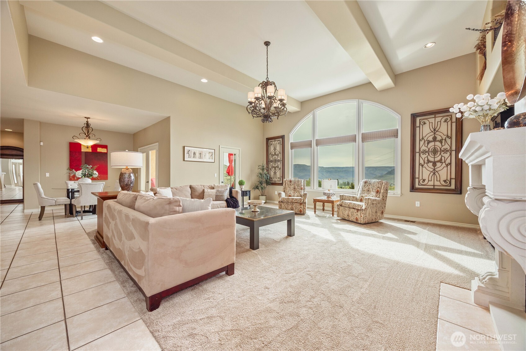 This spacious great room showcases an elegant blend of comfort and sophistication, highlighted by soaring ceilings and expansive windows that capture stunning natural light and scenic views. The open layout is perfect for both relaxing and entertaining, featuring plush seating areas, refined finishes, and a statement chandelier that adds a touch of timeless charm. A cozy fireplace anchors the space, while architectural details and built-in features enhance the home’s character and warmth. Seamlessly connected to the rest of the living areas, this inviting space is designed for effortless everyday living and memorable gatherings.