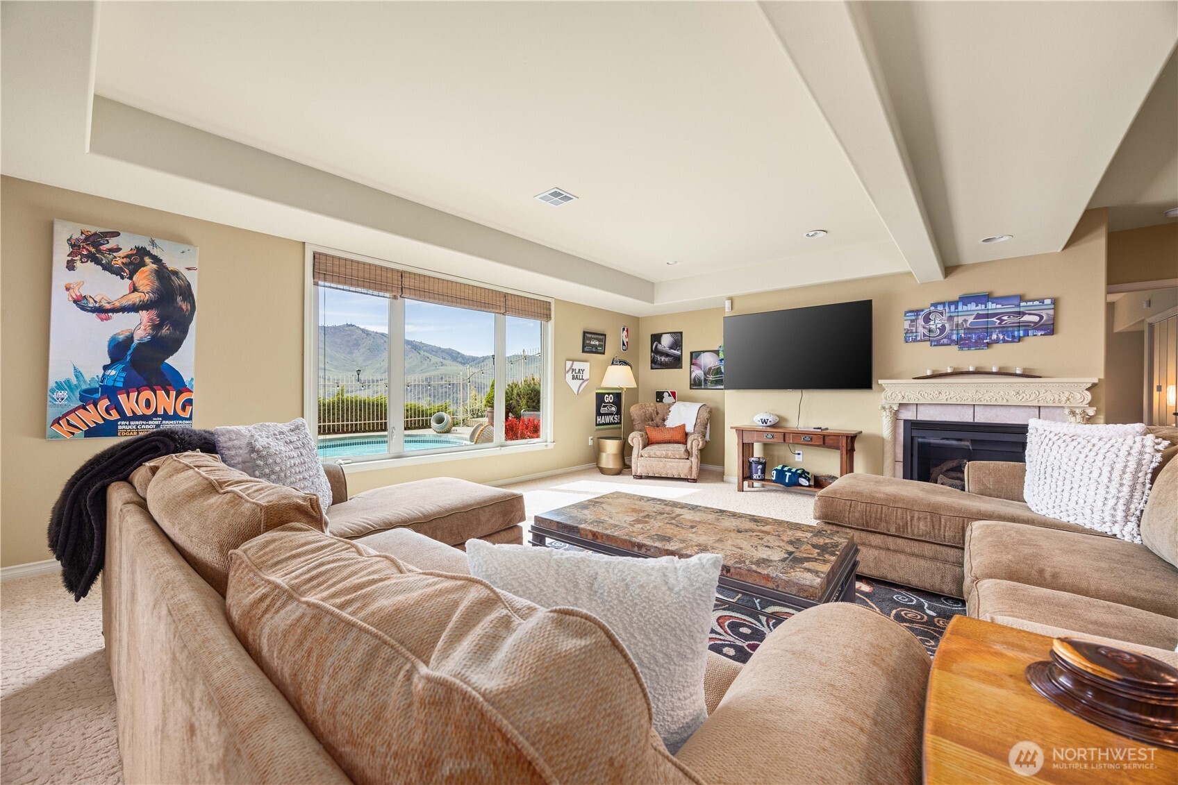 Comfortable and versatile lower-level living space designed for relaxation and entertaining, featuring a spacious seating area and abundant natural light from large windows overlooking the pool and capturing scenic views beyond. The open layout allows for flexible use as a media room, guest retreat, or additional living area, while warm finishes and thoughtfully arranged furnishings create an inviting atmosphere. Seamlessly connected to the rest of the home, this space offers both comfort and functionality for everyday living.