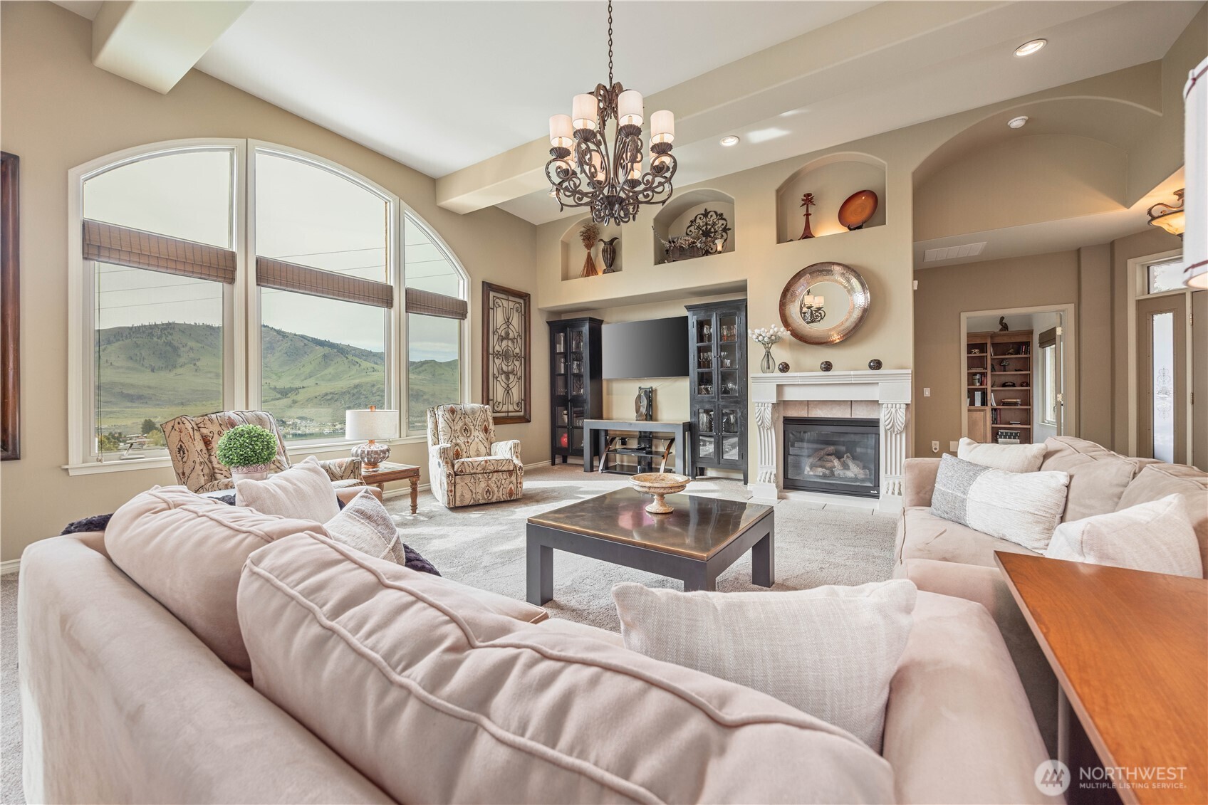 The inviting great room is filled with natural light, highlighted by expansive windows that frame picturesque territorial views. Soaring ceilings and elegant architectural details create a sense of openness, while the cozy fireplace with classic mantel serves as a warm focal point. The thoughtfully arranged seating area offers comfort and functionality, ideal for both everyday living and entertaining. Built-in niches and cabinetry add character and display space, while the seamless flow to adjacent living areas enhances the home’s open-concept design.