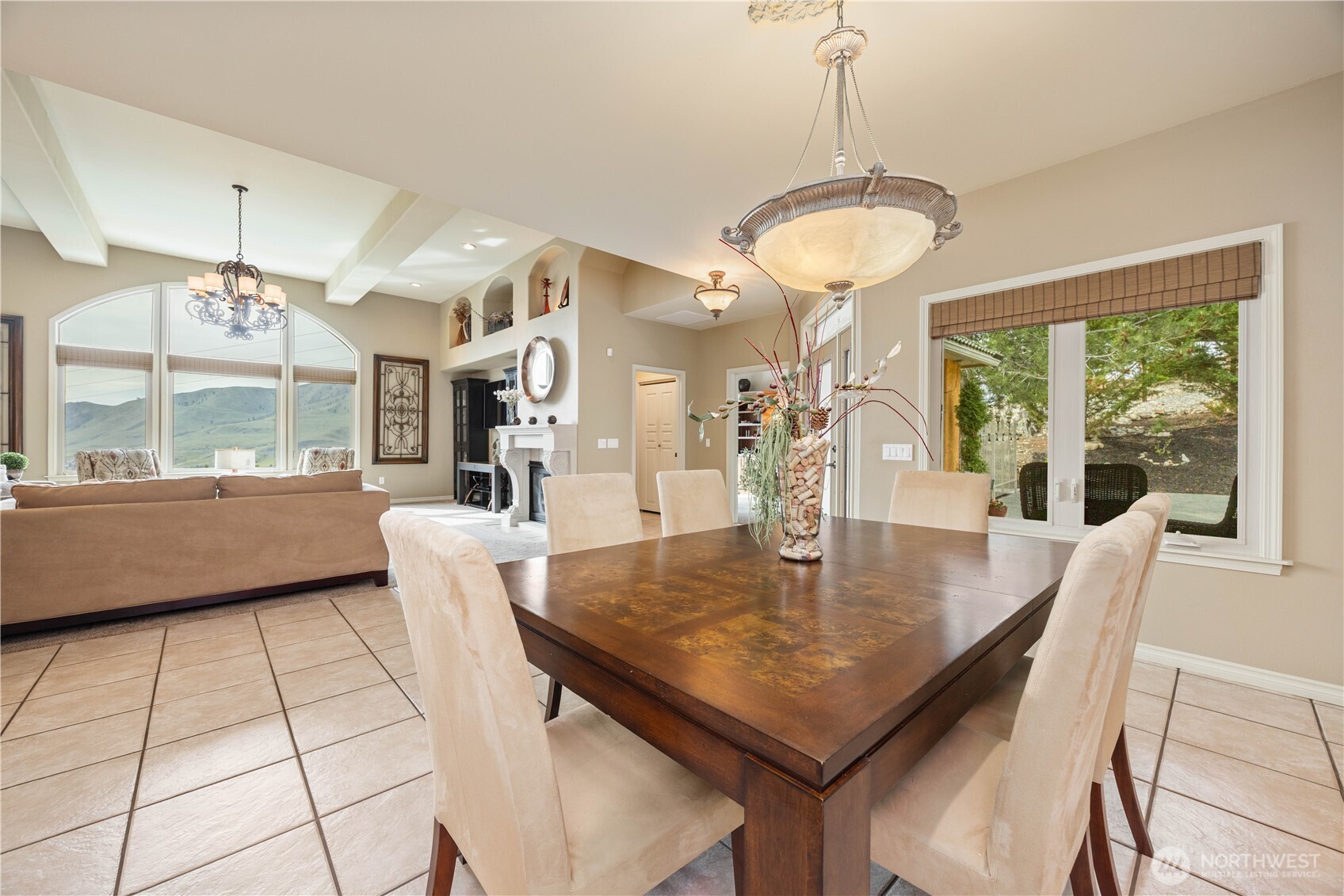 Elegant formal dining room designed for both intimate dinners and larger gatherings, featuring a striking wood dining table and ample seating. Expansive windows fill the space with natural light while capturing scenic views, creating a warm and inviting atmosphere. The refined chandelier adds a touch of sophistication, and the seamless connection to adjacent living spaces enhances flow for effortless entertaining.