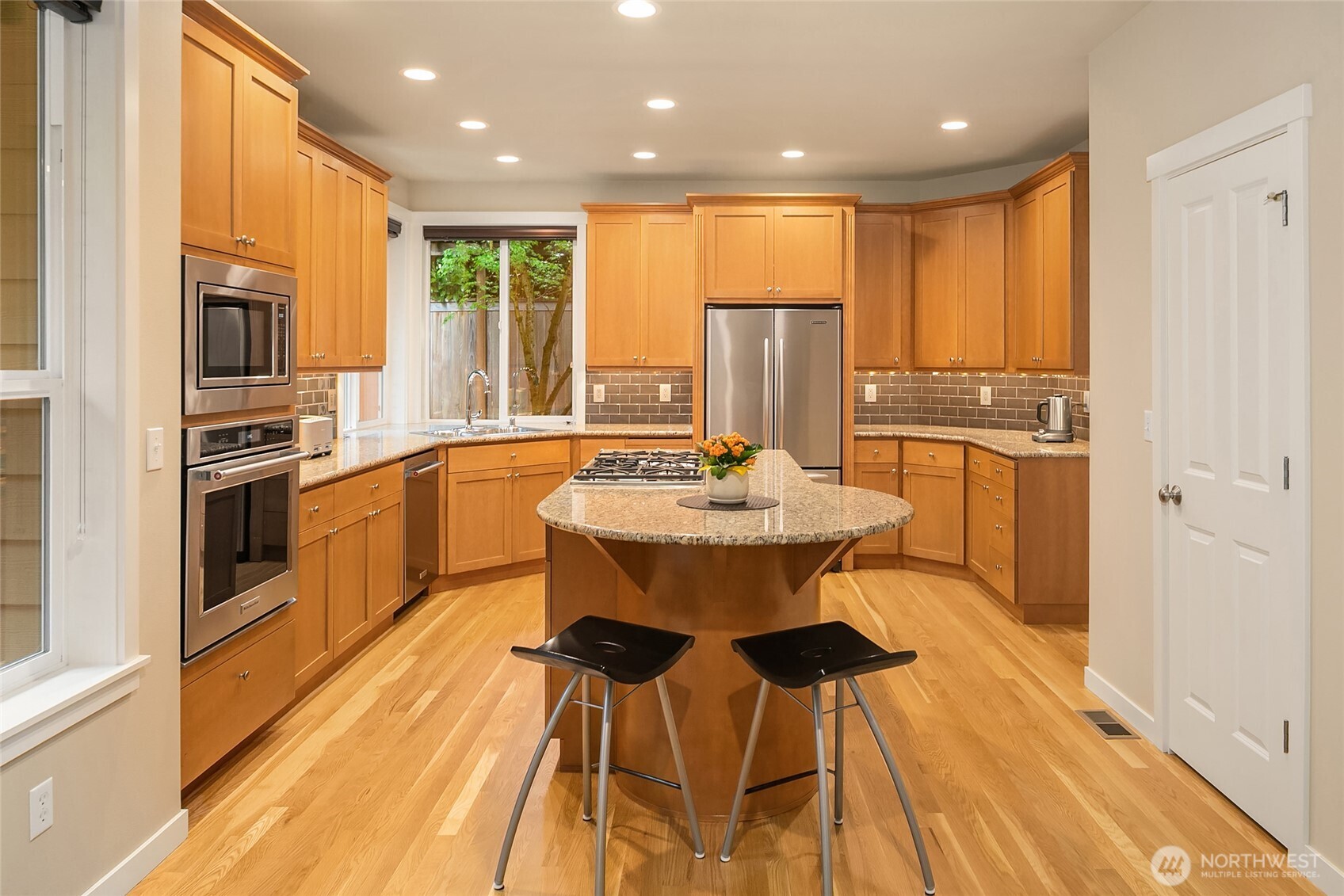 The kitchen features a statement center island with gas cooktop, granite countertops, newer backsplahs, premium stainless KitchenAid appliances, and generous space for casual dining.