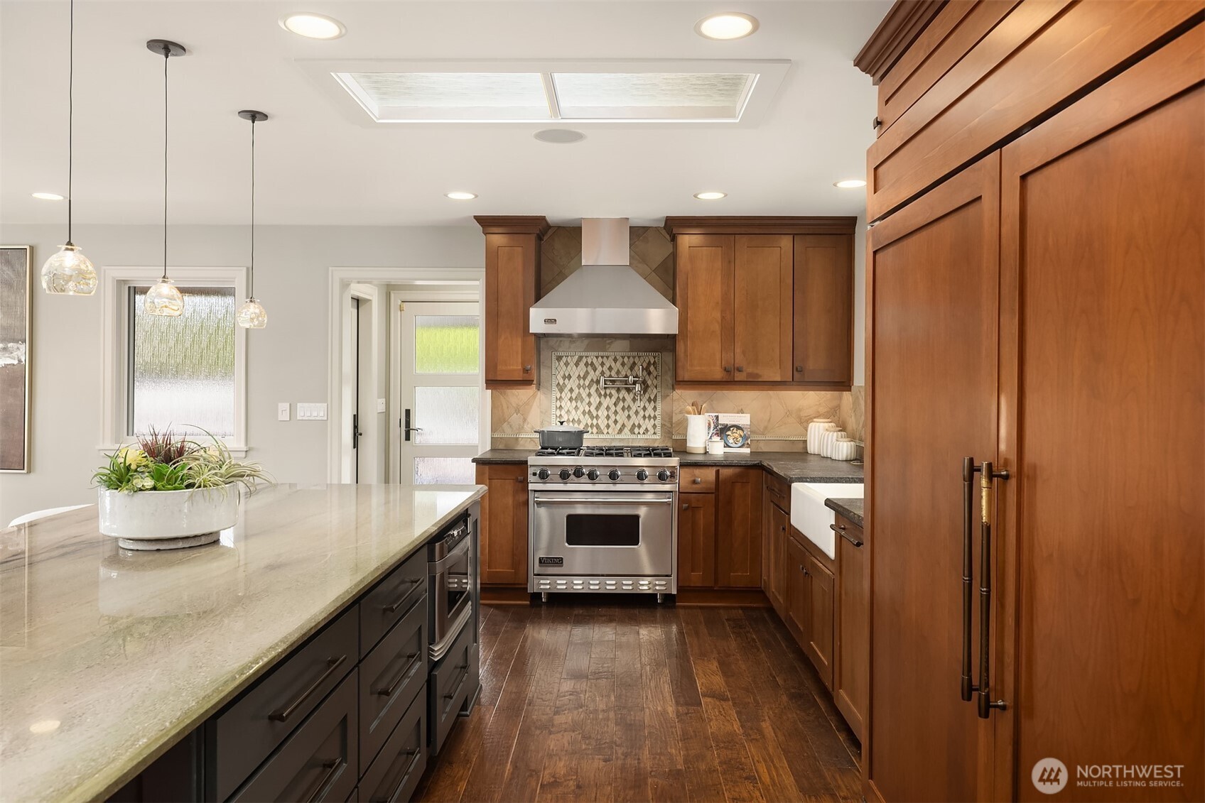 Designed to gather, the oversized island—finished in slate shaker cabinetry—offers generous prep space, casual seating, and effortless connection. A Sub-Zero refrigerator, GE Profile dishwasher, and Sharp microwave drawer bring quiet performance behind the scenes.