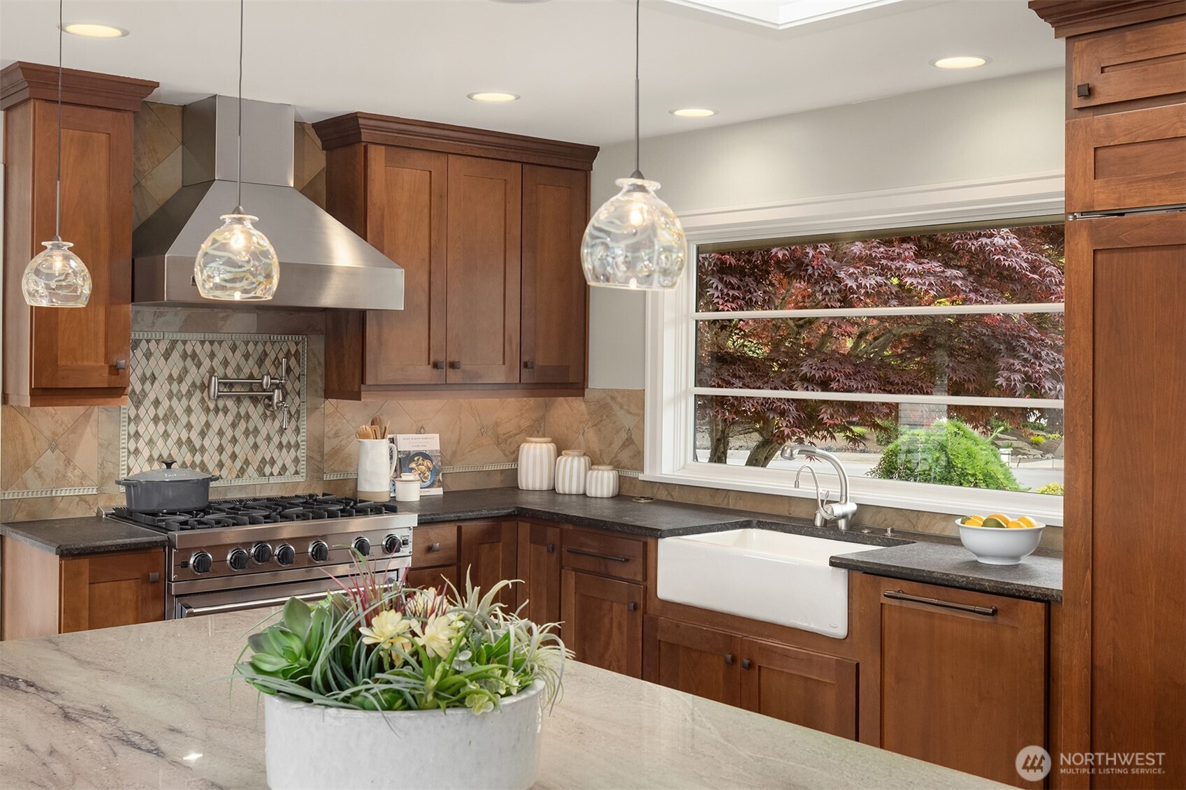 A kitchen built for serious cooking—anchored by a Viking 6-burner gas range, Viking hood, and pot filler, with a porcelain farmhouse sink set beneath natural light. Grohe fixtures, quartz countertops, and warm shaker cabinetry elevate every detail.
