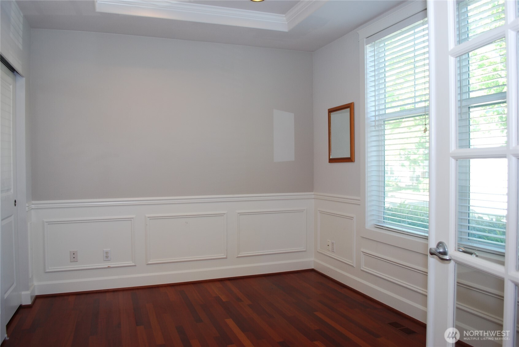 Brazilian cherry hardwood floors flow past the glass panel French doors in the 9 foot coffered ceiling, half wall panel style den.