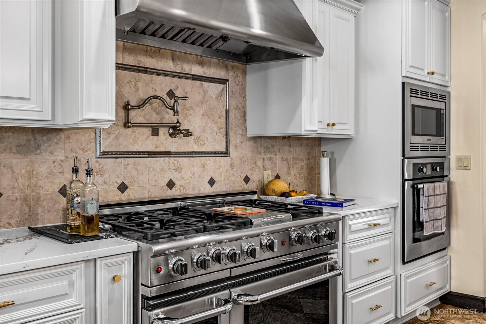 Main Floor Kitchen: Detailed view of the professional range, custom hood, and elegant tile backsplash.