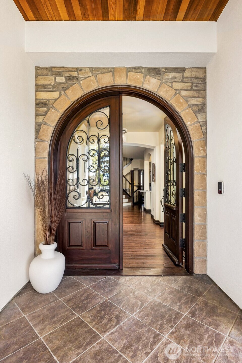 Front Entry: Dramatic arched wood door framed by stone tile and warm architectural detailing.