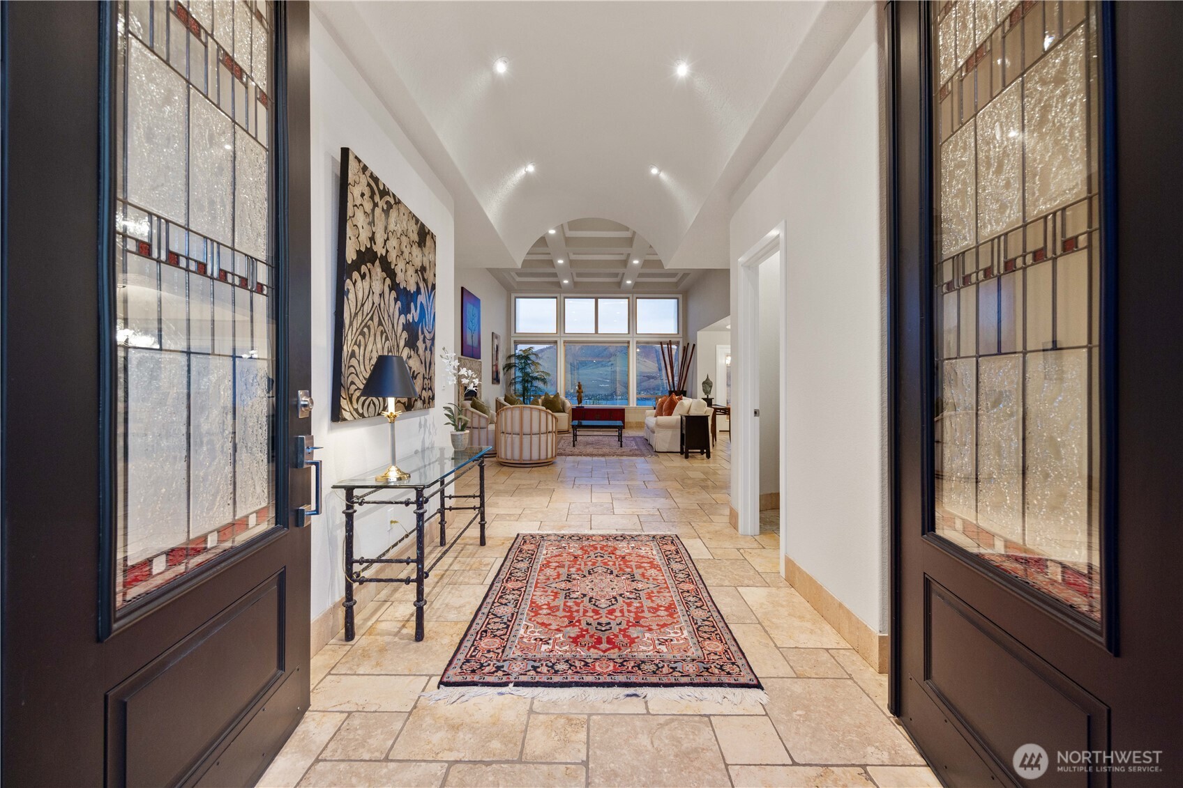 Grand, light-filled entry sets the tone with soaring ceilings, rich accents, and elegant double doors. A long, inviting hallway draws you in with warm natural light, art niches, and a statement runner, creating a refined first impression and seamless transition into the home’s main living spaces.