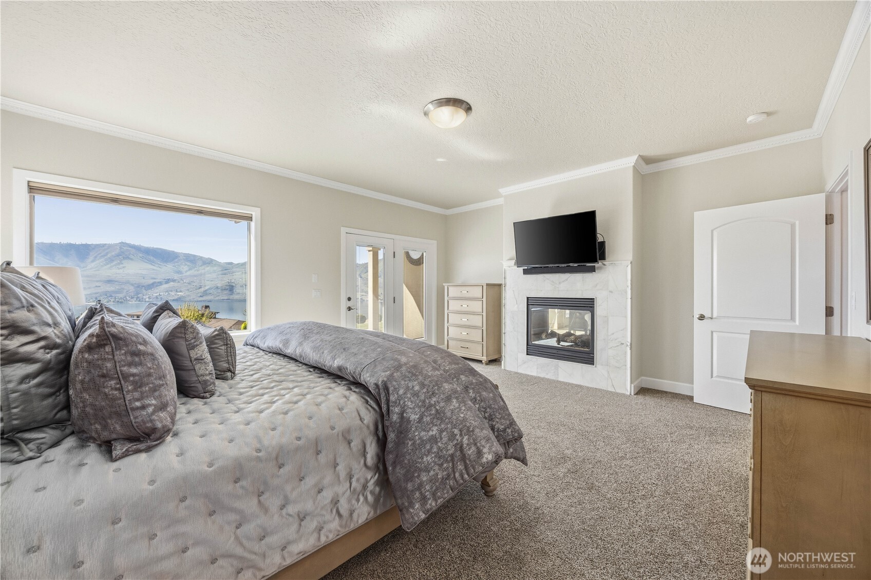 Bright and comfortable primary suite featuring soft neutral tones, plush carpeting, and abundant natural light. A cozy gas fireplace adds warmth and ambiance, while the generous layout and ample closet space create a welcoming and functional retreat.