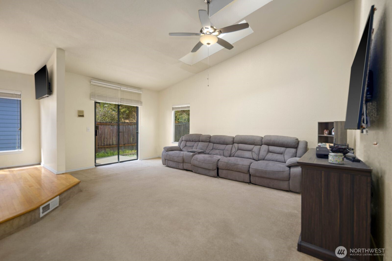 Living area with vaulted ceiling, ceiling fan, and sliding door providing access to the backyard