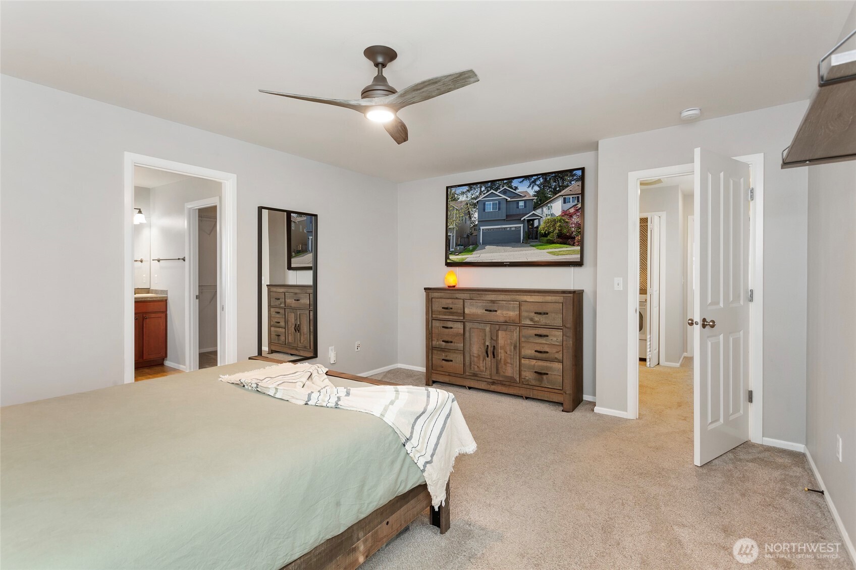 Alternate view of the expansive primary suite showcasing the impressive room size and flexible layout. Plush carpeting, soft neutral tones, and a ceiling fan enhance comfort and relaxation. Clear sightlines highlight the convenient access to the adjacent en-suite bath and spacious walk-in closet, reinforcing this bedroom’s true suite-style design with plenty of room to unwind and personalize.