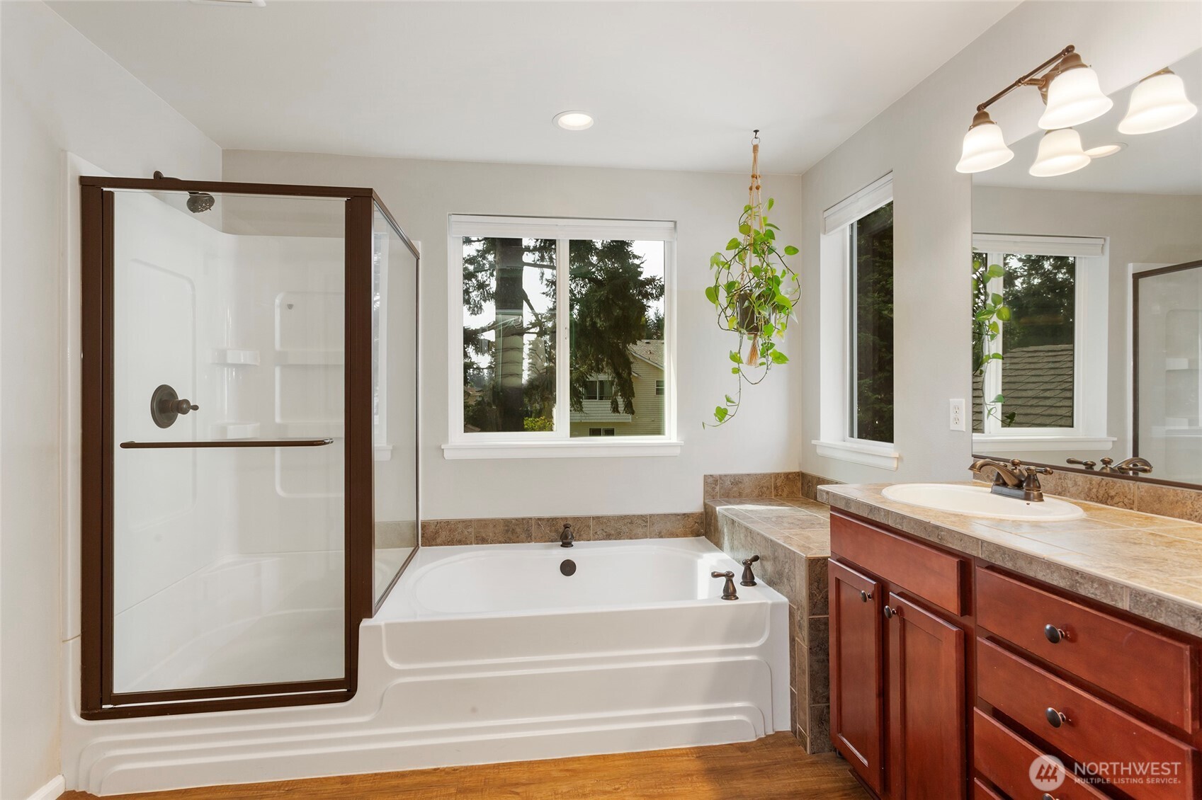 Primary bathroom retreat featuring a well-designed layout with both a soaking tub and a separate walk-in shower, offering flexibility and comfort. Warm wood cabinetry, a spacious vanity with ample counter space, and classic tile accents add timeless appeal. Large windows bring in natural light, creating a bright, relaxing atmosphere ideal for unwinding at the end of the day.