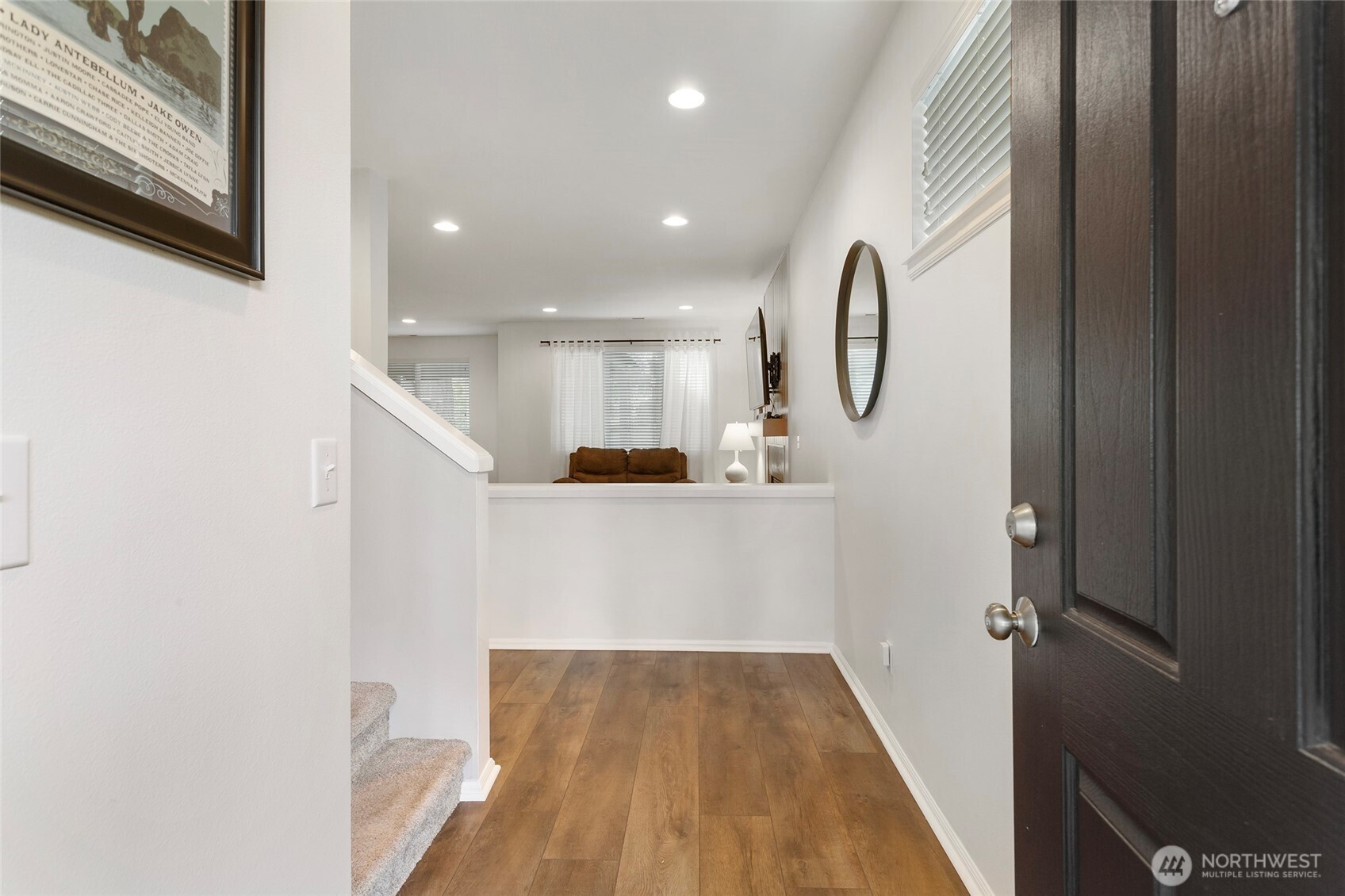 Bright and welcoming entryway featuring warm wood LVP flooring, recessed lighting, and crisp white walls that create a clean, modern first impression. The open sightline to the living area and adjacent staircase adds a sense of flow and spaciousness from the moment you enter.
