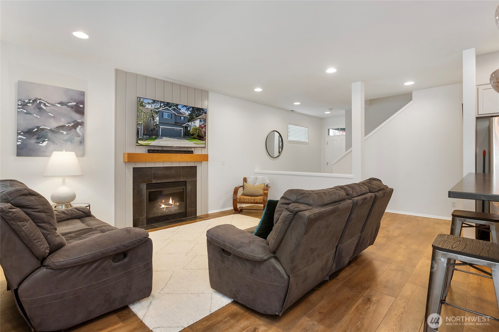 Inviting living room perspective showcasing the open connection to the entryway, hallway, and stairwell. Recessed lighting, warm LVP floors, and a thoughtful layout highlight the home’s natural flow, making the space feel bright, open, and easily connected throughout the main level.