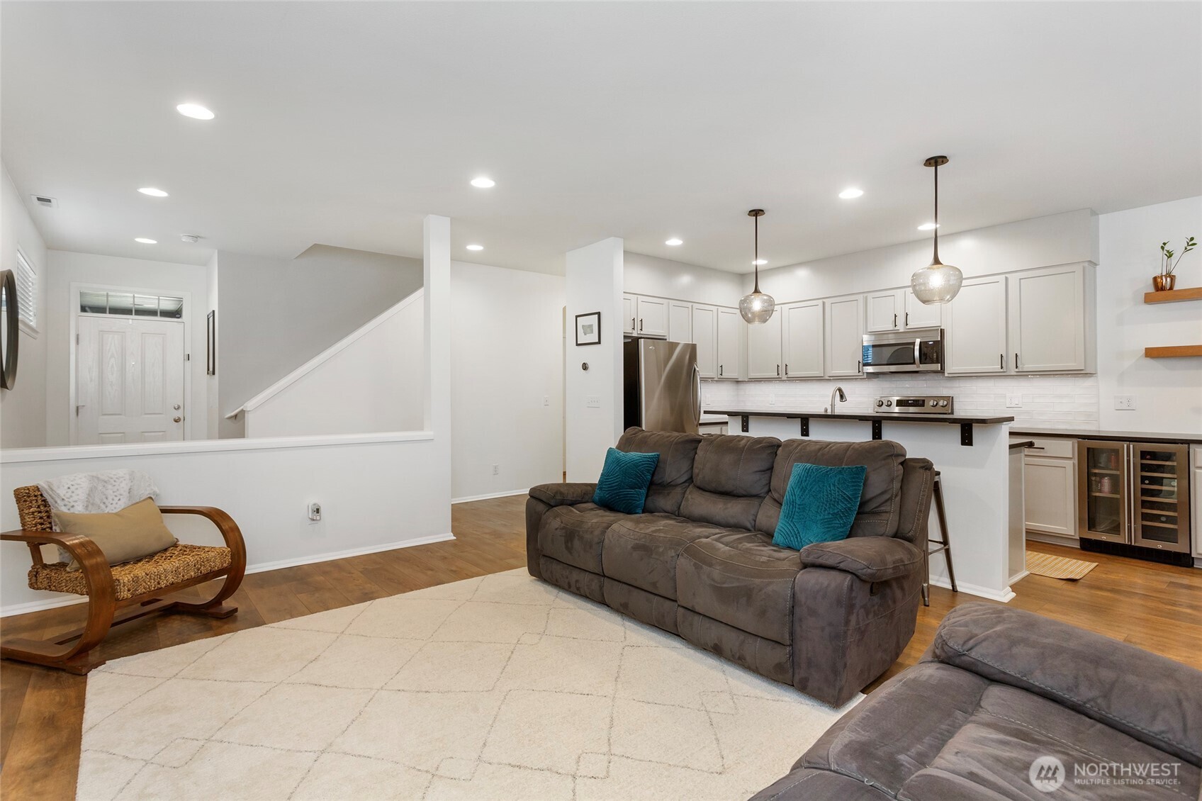 Expansive open-concept view capturing the seamless connection between the living room, kitchen, entryway, and stairwell. LVP floors, recessed lighting, and pendant lights over the breakfast bar enhance the bright, modern feel while showcasing the home’s effortless flow and functional layout—perfect for gathering and entertaining.