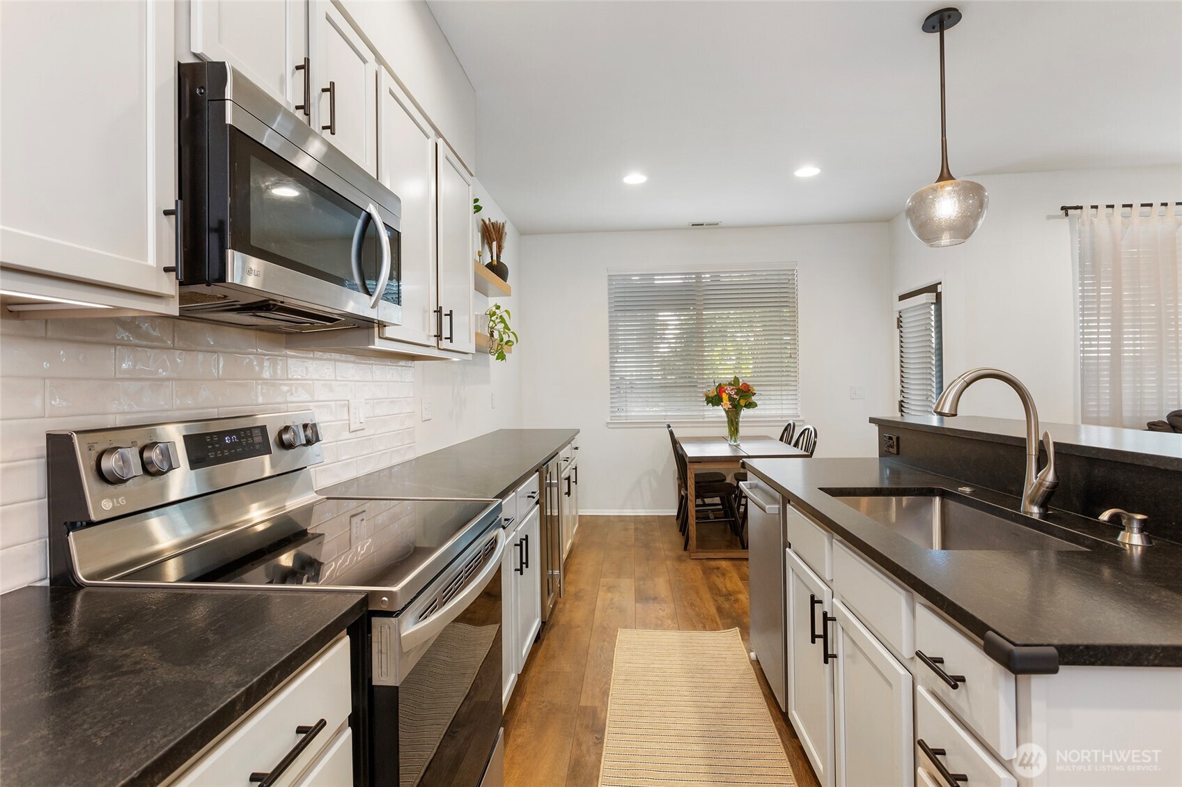 Another bright kitchen view highlighting the galley-style layout with granite countertops, stainless steel appliances, and modern cabinetry. Durable LVP flooring flows throughout, while recessed and pendant lighting enhance the clean, modern design and provide a clear sightline to the dining area—ideal for both everyday use and entertaining.