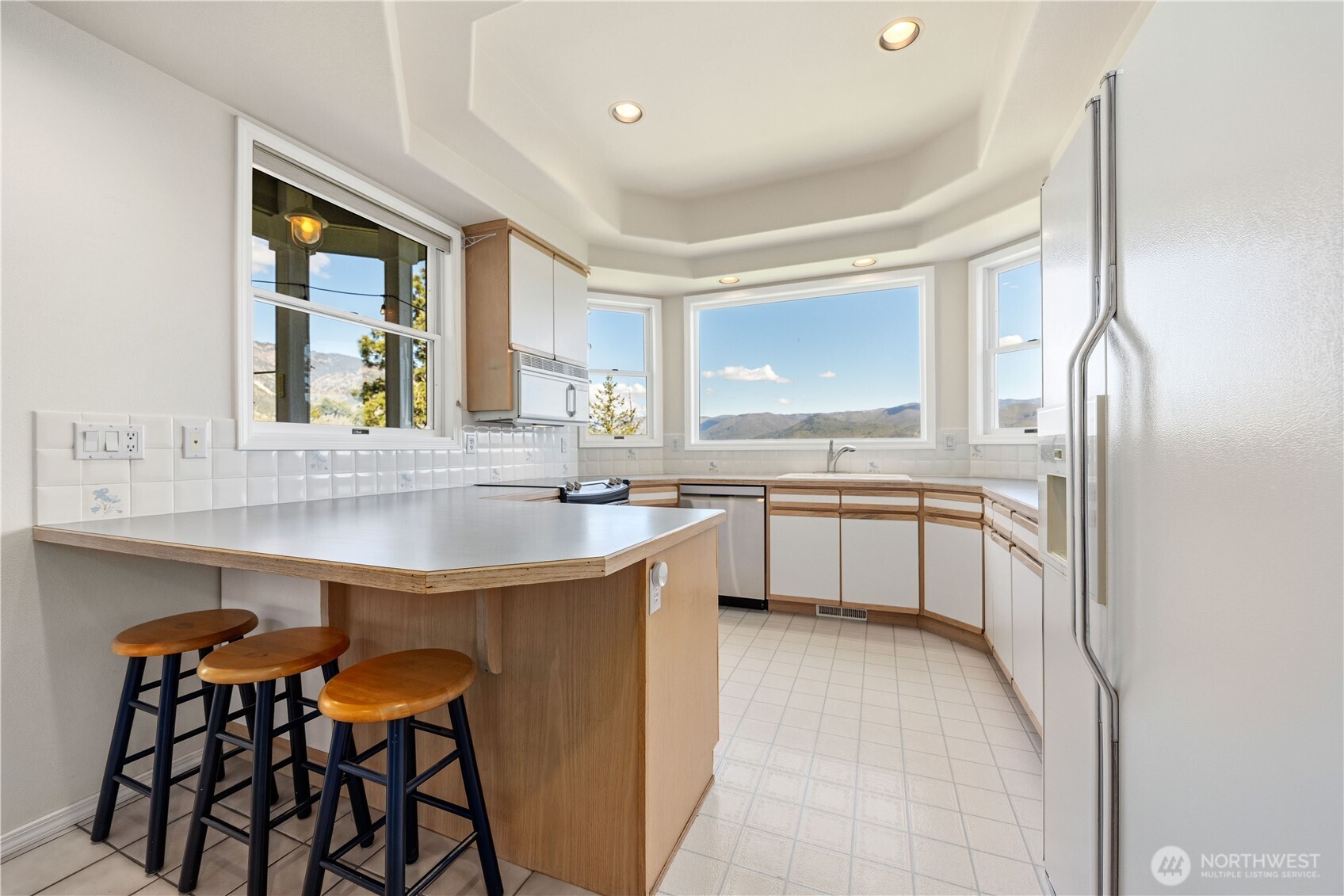 Bright kitchen with white cabinetry, ample counter space, and eating bar. Large windows wrap the space, filling it with natural light and offering epic lake views.