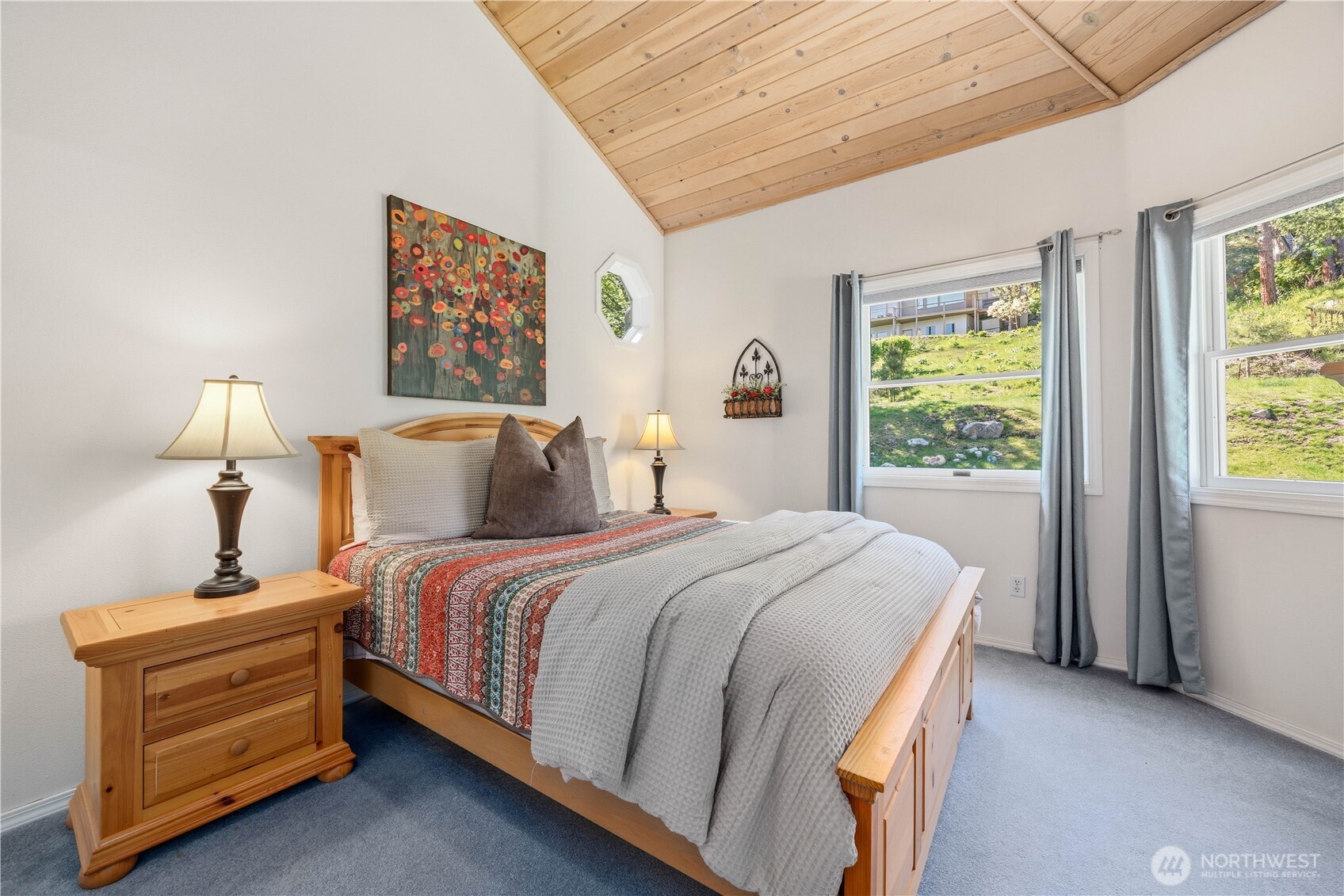 Guest Suite Bedroom with vaulted wood-paneled ceiling, great windows providing natural light and a glimpse at natural beauty this community provides. The space features neutral tones, wood furniture, and a comfortable layout.