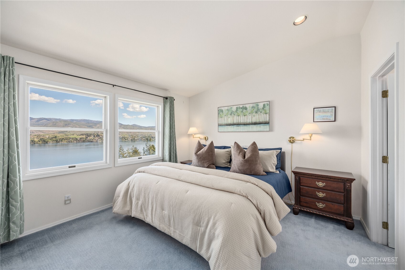Primary ensuite bedroom with large windows capturing expansive lake and mountain views. The space features neutral tones, soft natural light, and a clean, comfortable layout.