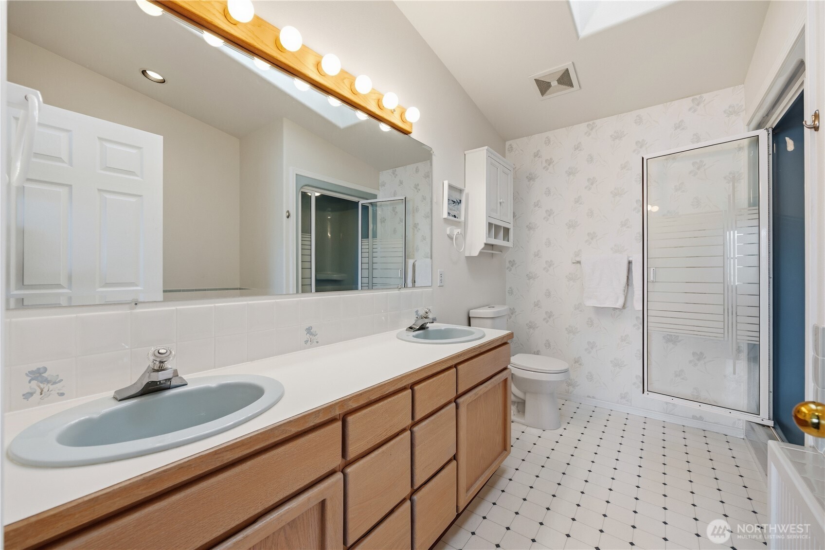 Primary bathroom with dual-sink vanity, wood cabinetry, and large mirror with overhead lighting. Features a enclosed shower, soaking tub, and bright, spacious layout.