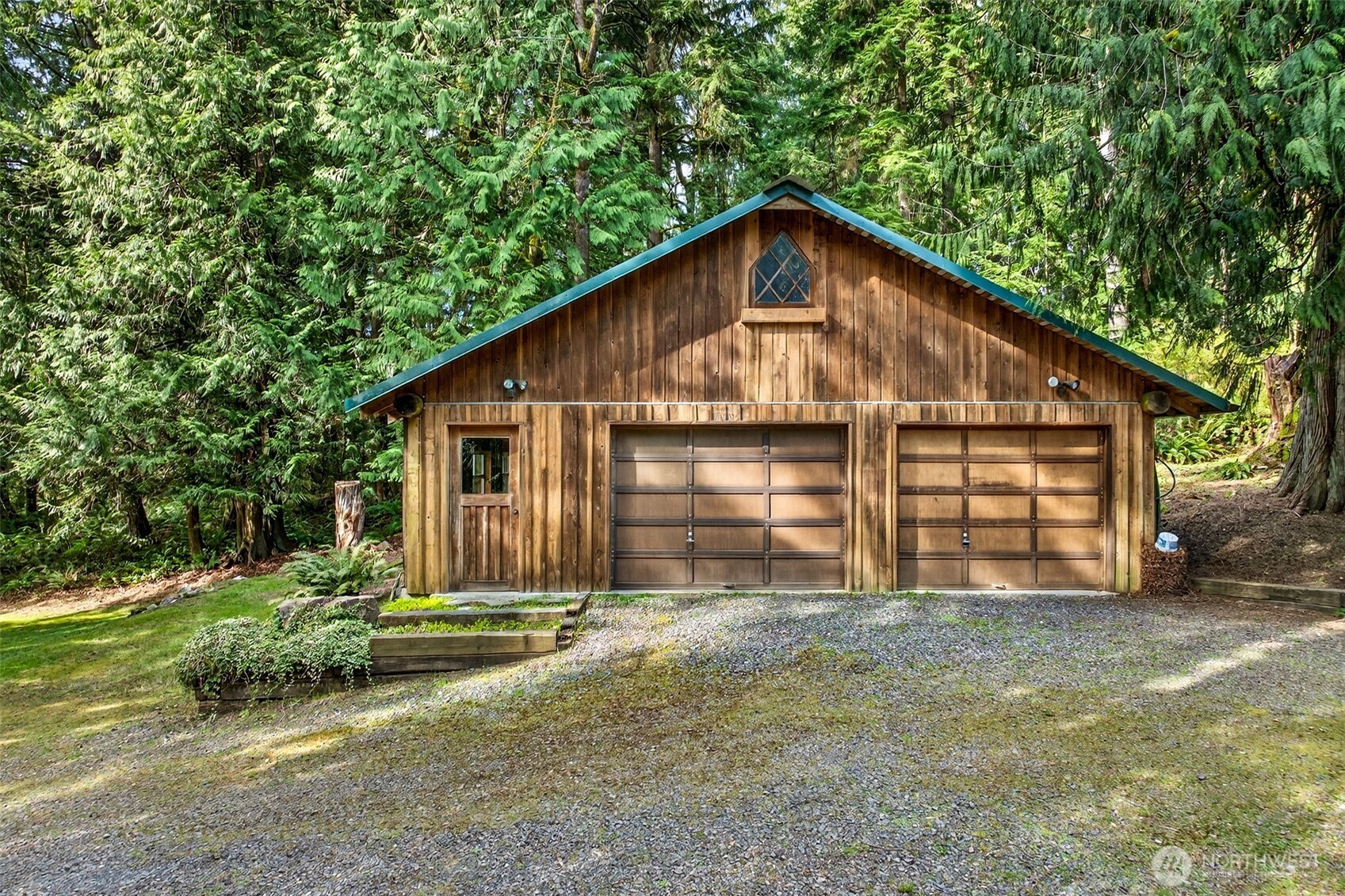 The detached two-car garage is a standout bonus — a beautifully crafted structure with matching green roof trim, a leaded diamond-pane gable window, and a pedestrian door, offering exceptional storage, workshop, or hobby space well beyond what most properties provide.