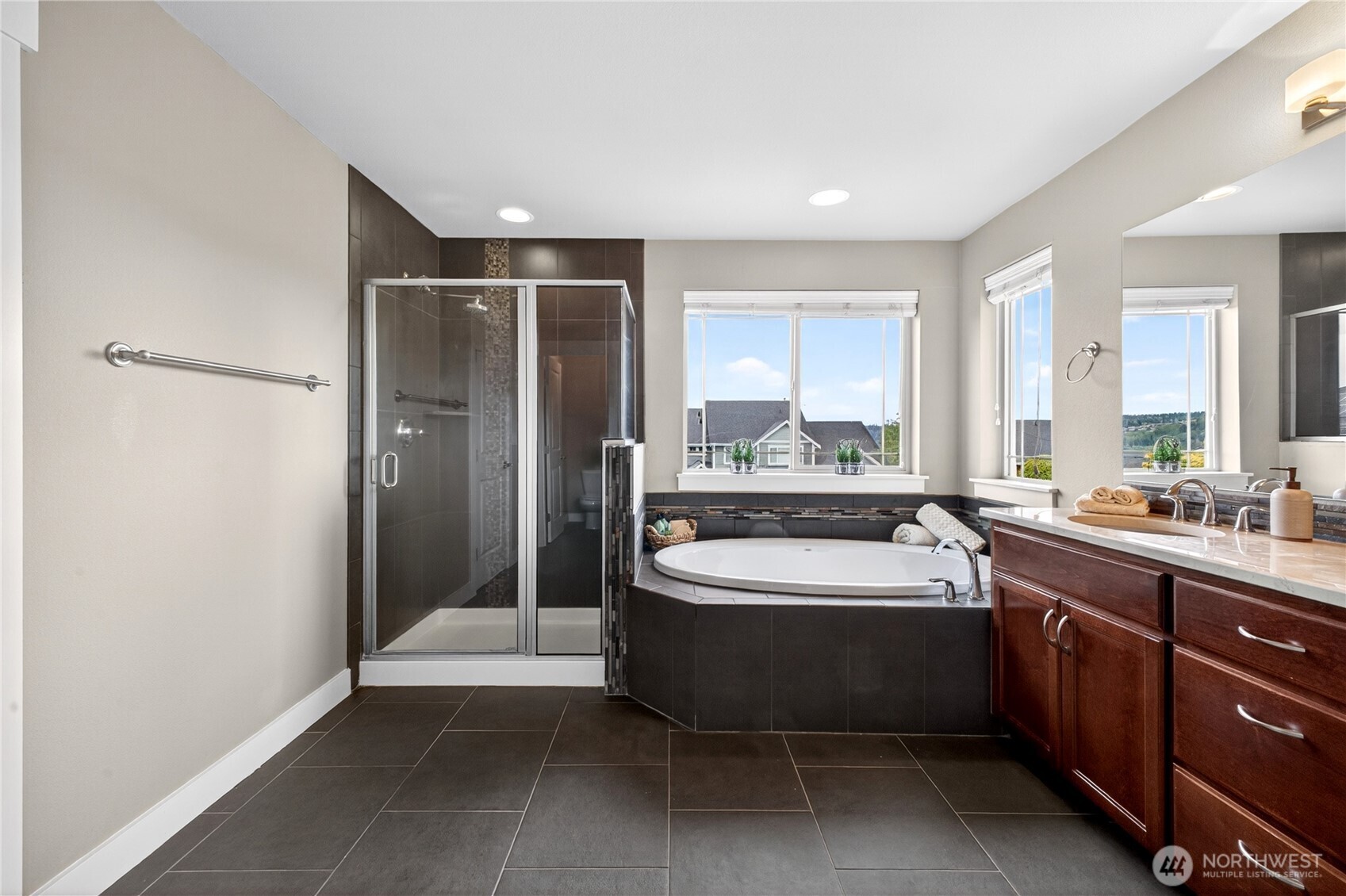 Primary bathroom offers a spa-like feel with a soaking tub, large tiled shower, double sinks with upgraded countertops, a private water closet, and abundant cabinet and counter space.