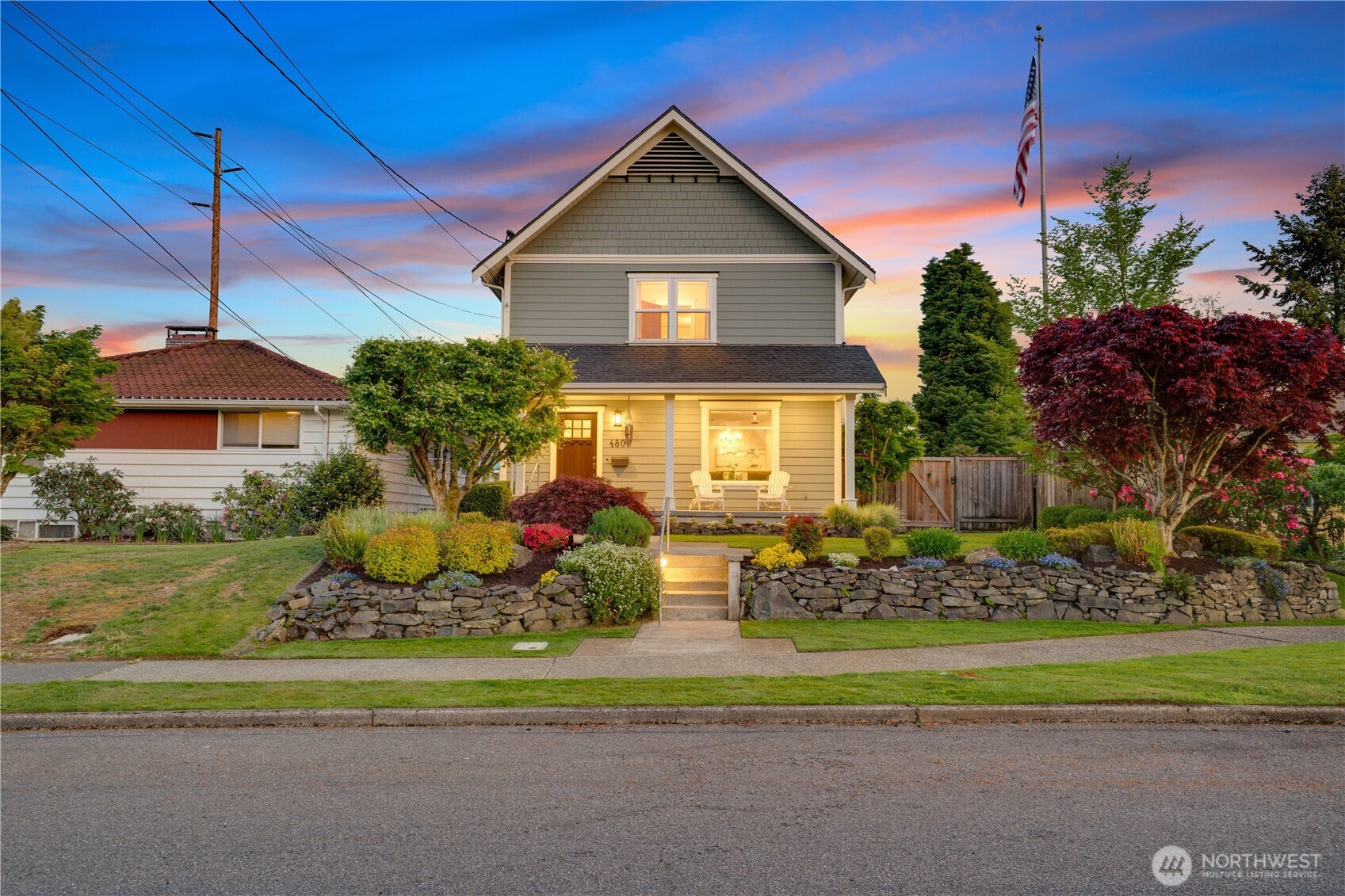 Classic craftsman charm meets modern curb appeal — glowing porch lights, lush terraced gardens, and a breathtaking Pacific Northwest sunset sky welcome you home to 4806.