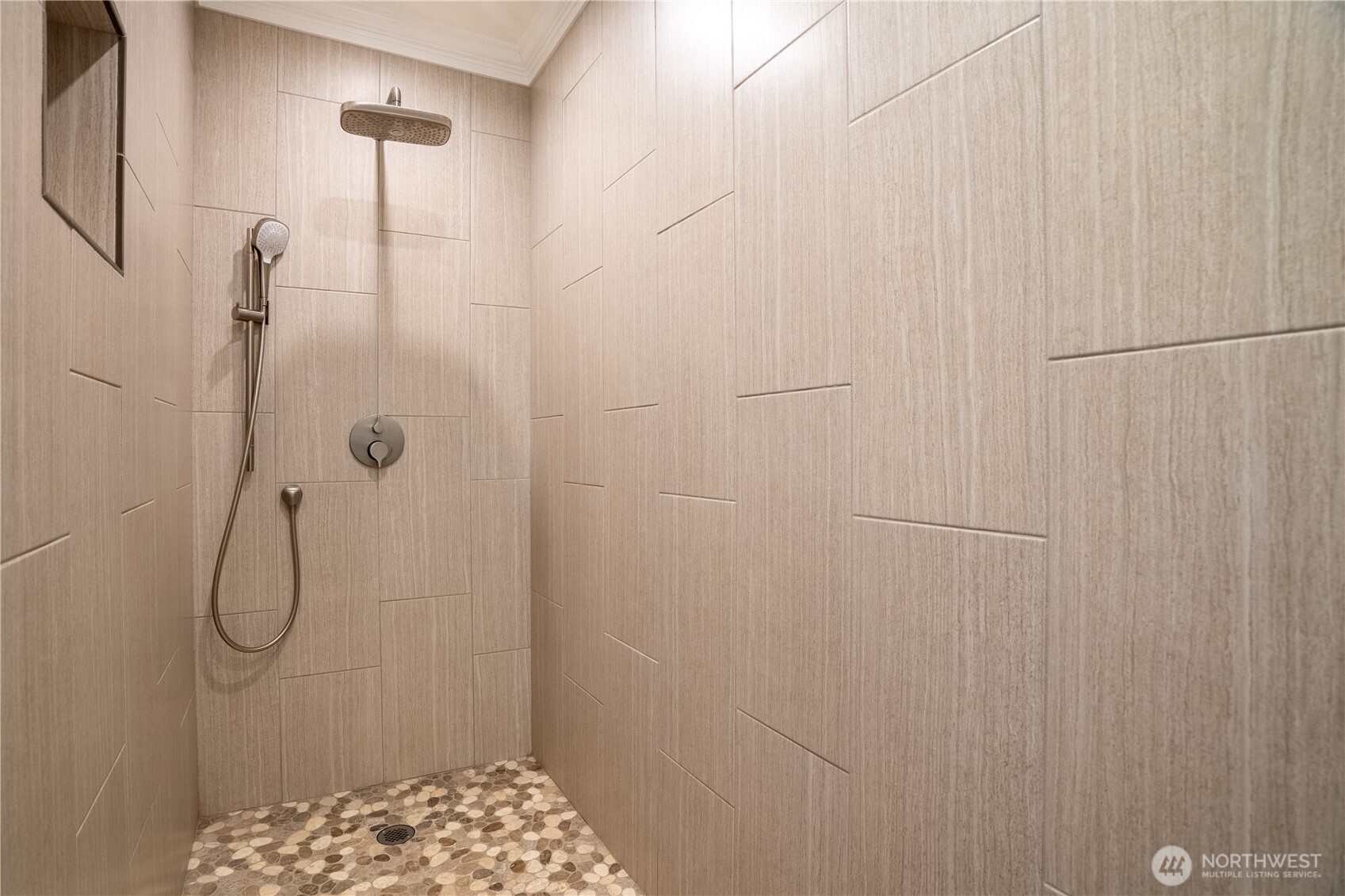Spa-inspired walk-in shower featuring a ceiling-mount rain head, hand-held wand, designer brushed nickel fixtures, and stunning pebble stone mosaic floor — a true daily retreat.